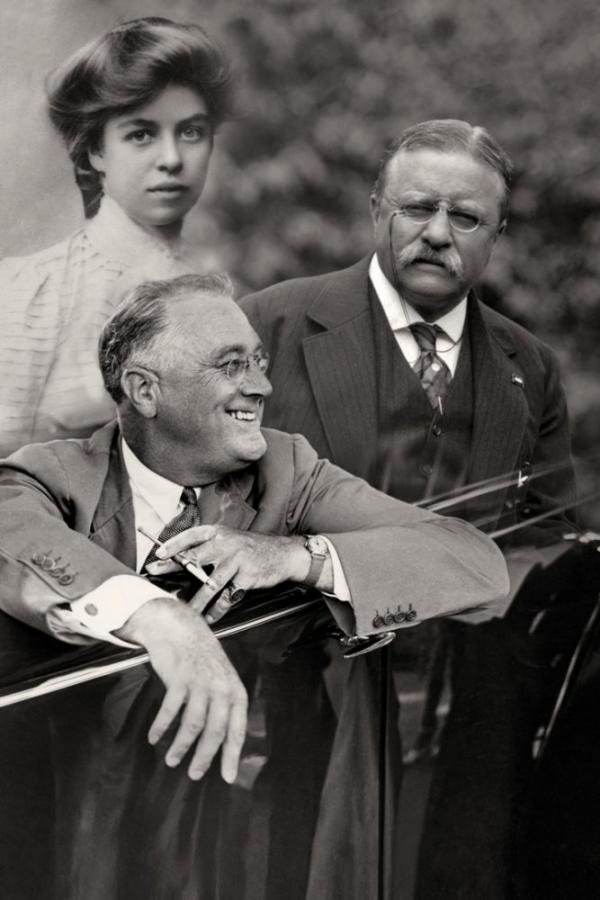 Three people, two men and one woman, outdoors in a black-and-white photograph. The man in the foreground is smiling, wearing glasses and a suit. The man behind him is looking at him with a serious expression, also in a suit. The woman is in the background, looking at the camera with a neutral expression.