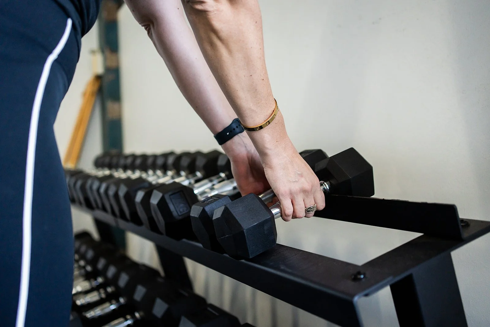 Person lifting a dumbbell on a black exercise rack in a gym.