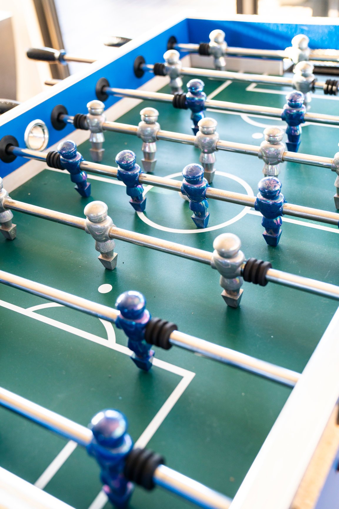 Foosball table with blue and silver player figures on a green playing field.