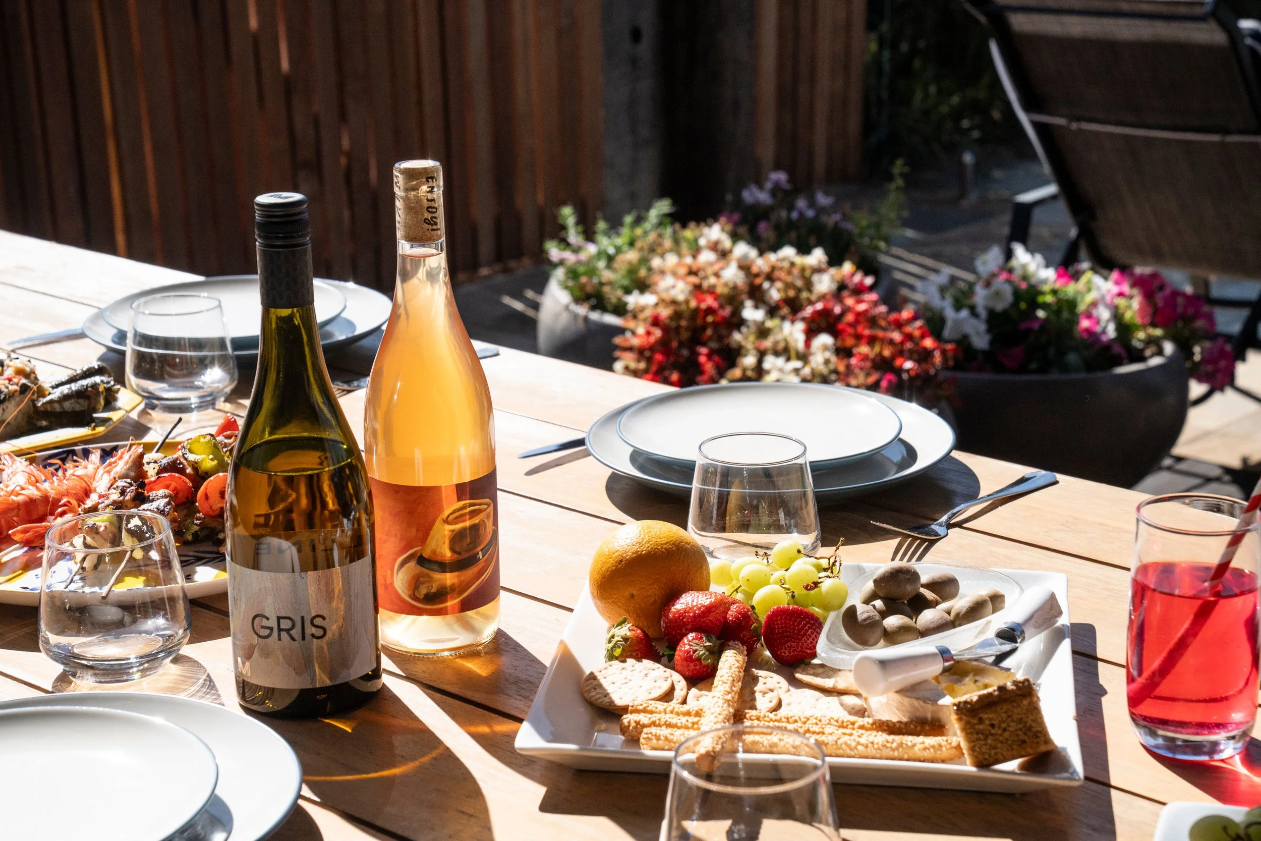 Outdoor dining table with wine, charcuterie, flowers, and empty plates.