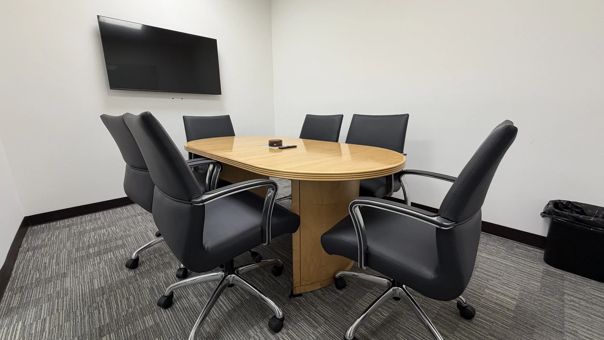 Modern office / conference room with a long wooden table and ergonomic office chairs, a whiteboard, and a screen.