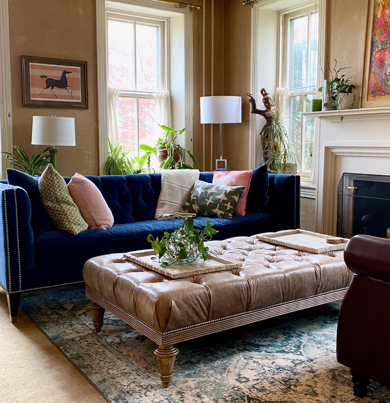 Blue velvet sofa with throw pillows and a tufted leather ottoman used as a coffee table.