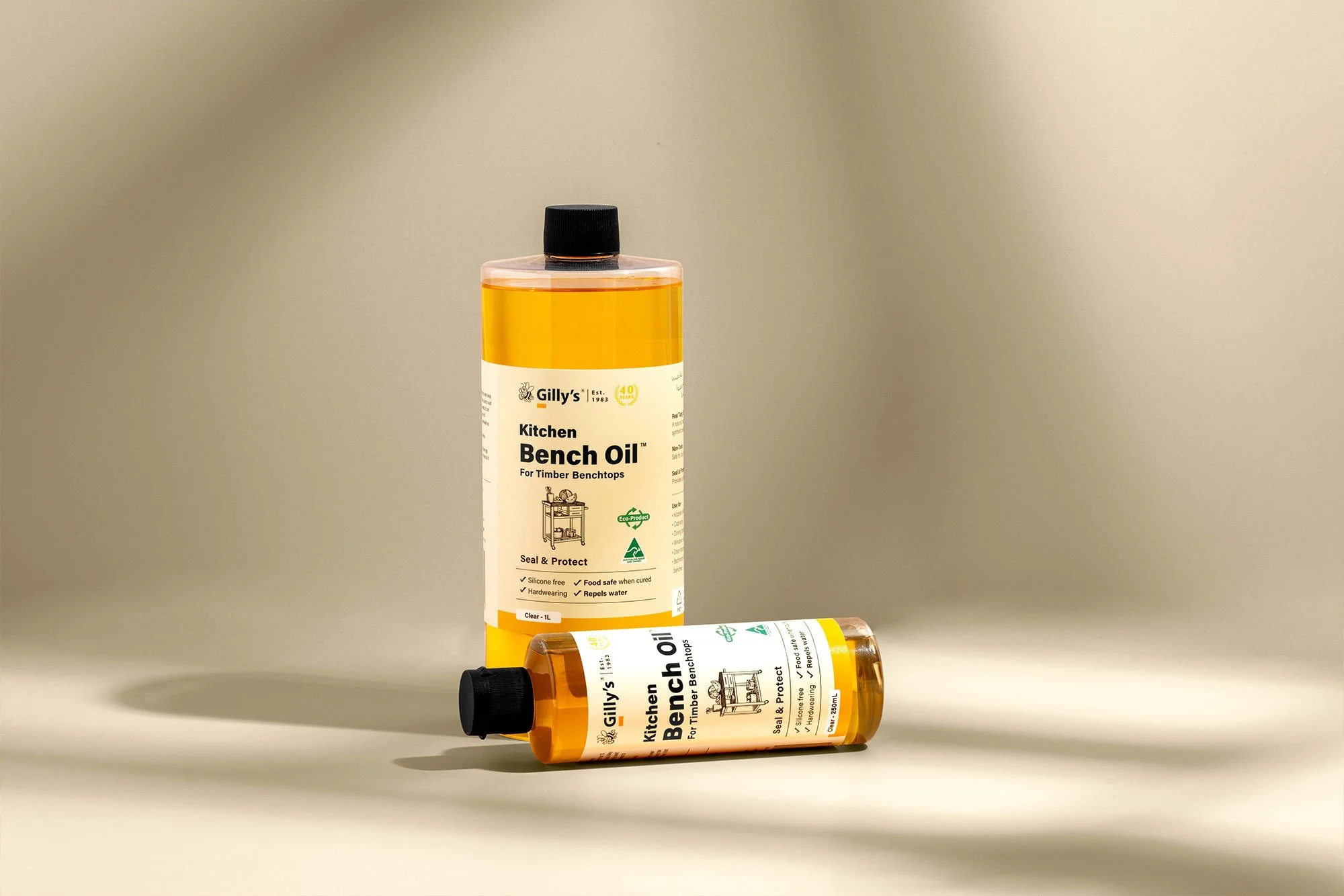 Two bottles of Gilly's Kitchen Bench Oil for timber benchtops on a beige background.