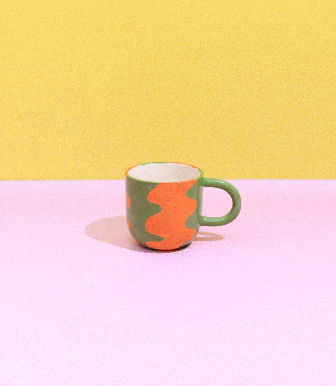 Colorful ceramic mug with green and orange pattern on pink and yellow background.