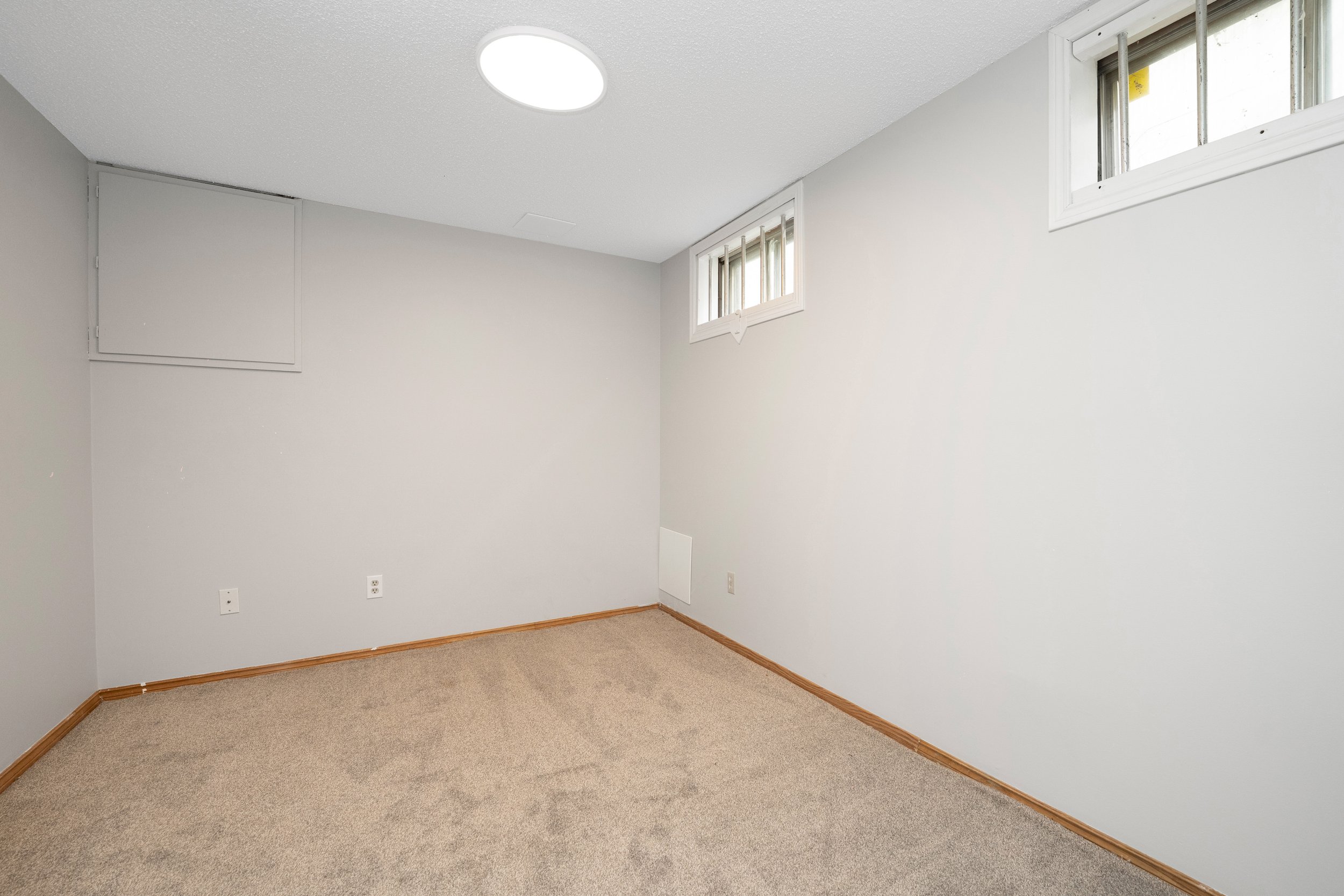 Empty basement room with beige carpet, white walls, small windows, and wood trim.