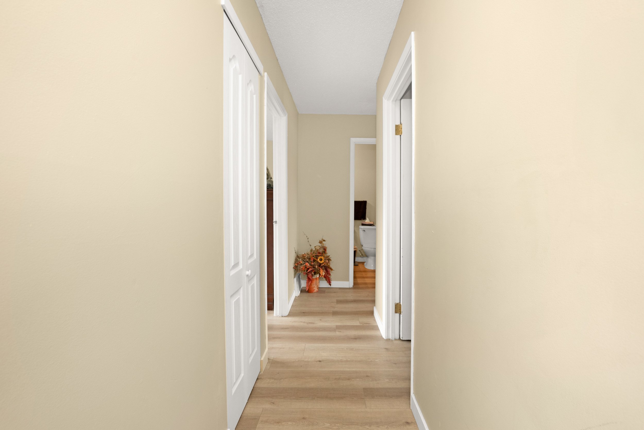 Long hallway leading to rooms with wooden flooring.