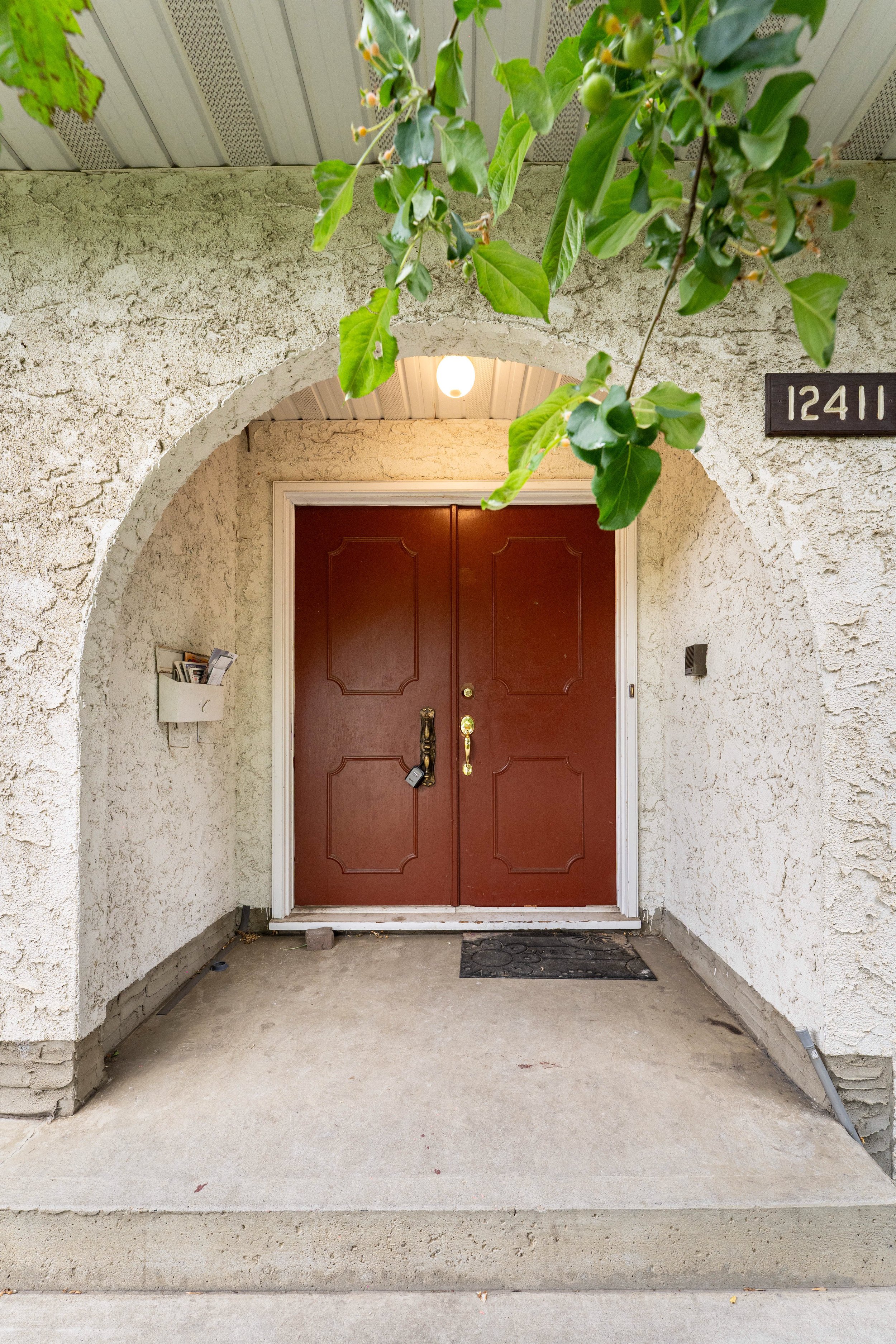 Front porch with a brown double door, house number 12411, mailbox, and greenery hanging overhead.