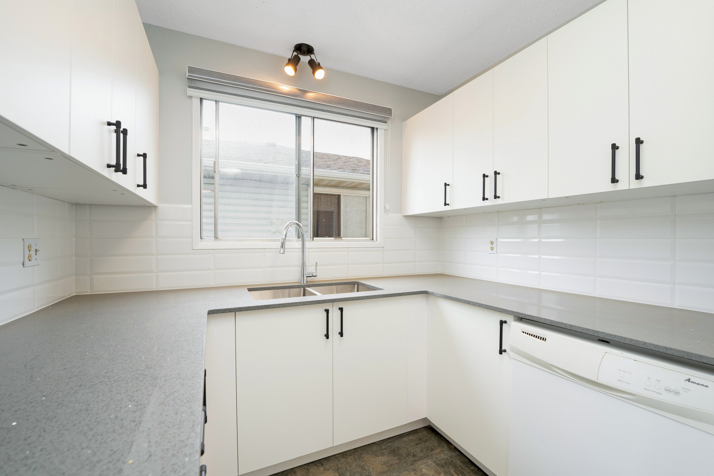 Modern U-shaped kitchen with white cabinets, gray countertops, a window above the sink, and a dishwasher.