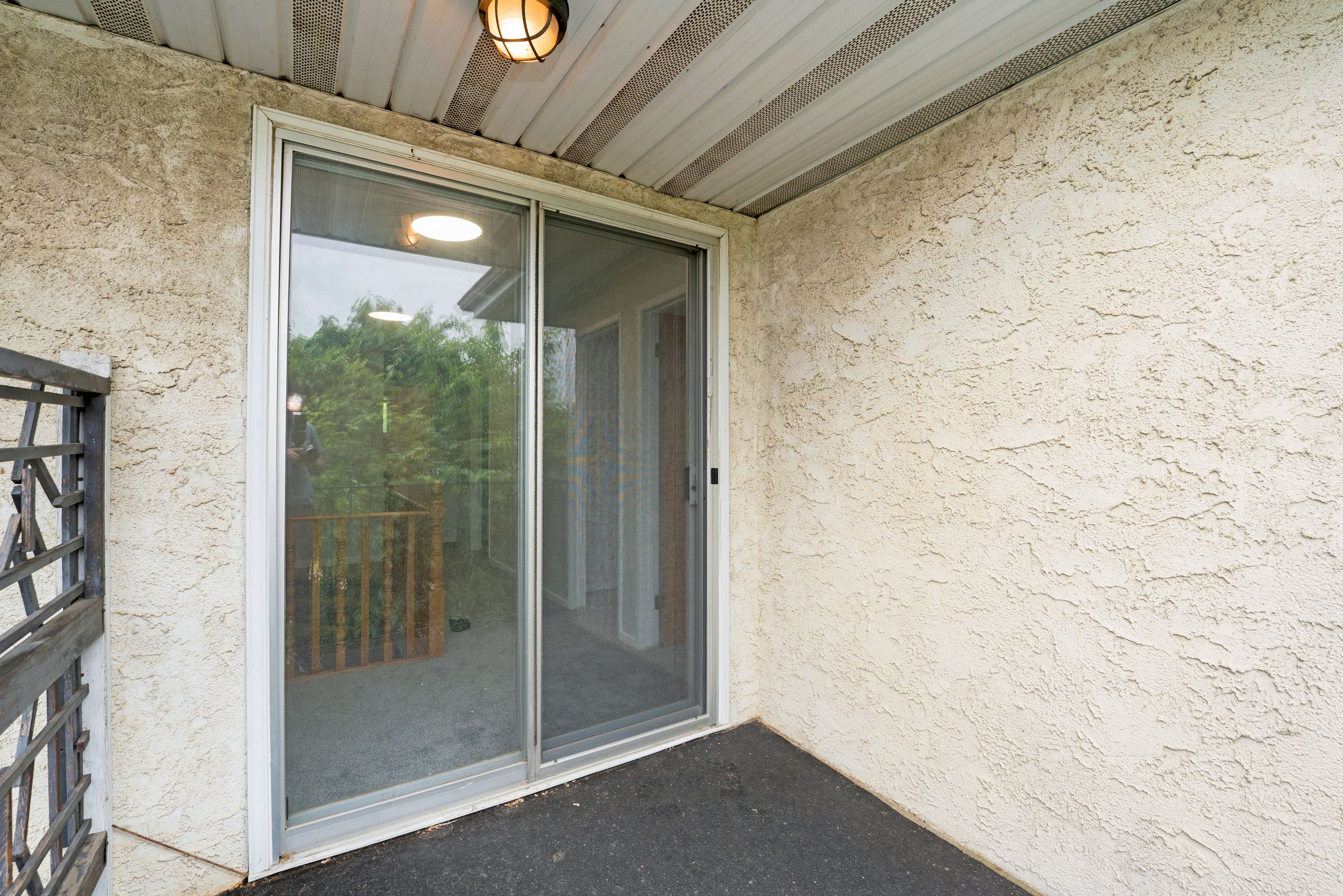 View of a balcony or patio area with a sliding glass door, beige stucco walls, and a tiled ceiling with two lights.