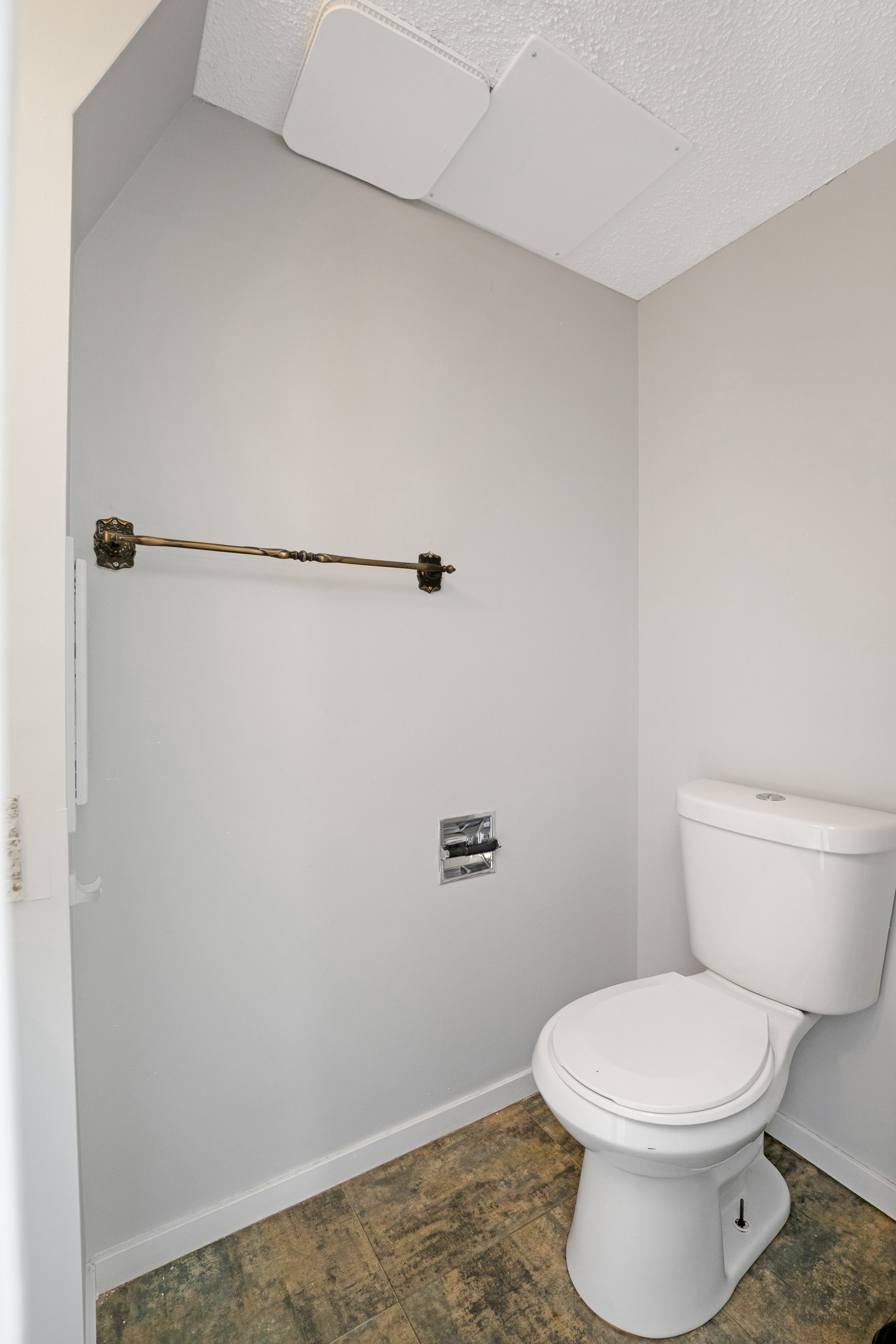 Empty bathroom with a toilet, a towel bar, a vent, and an opening for a toilet paper holder on the wall.