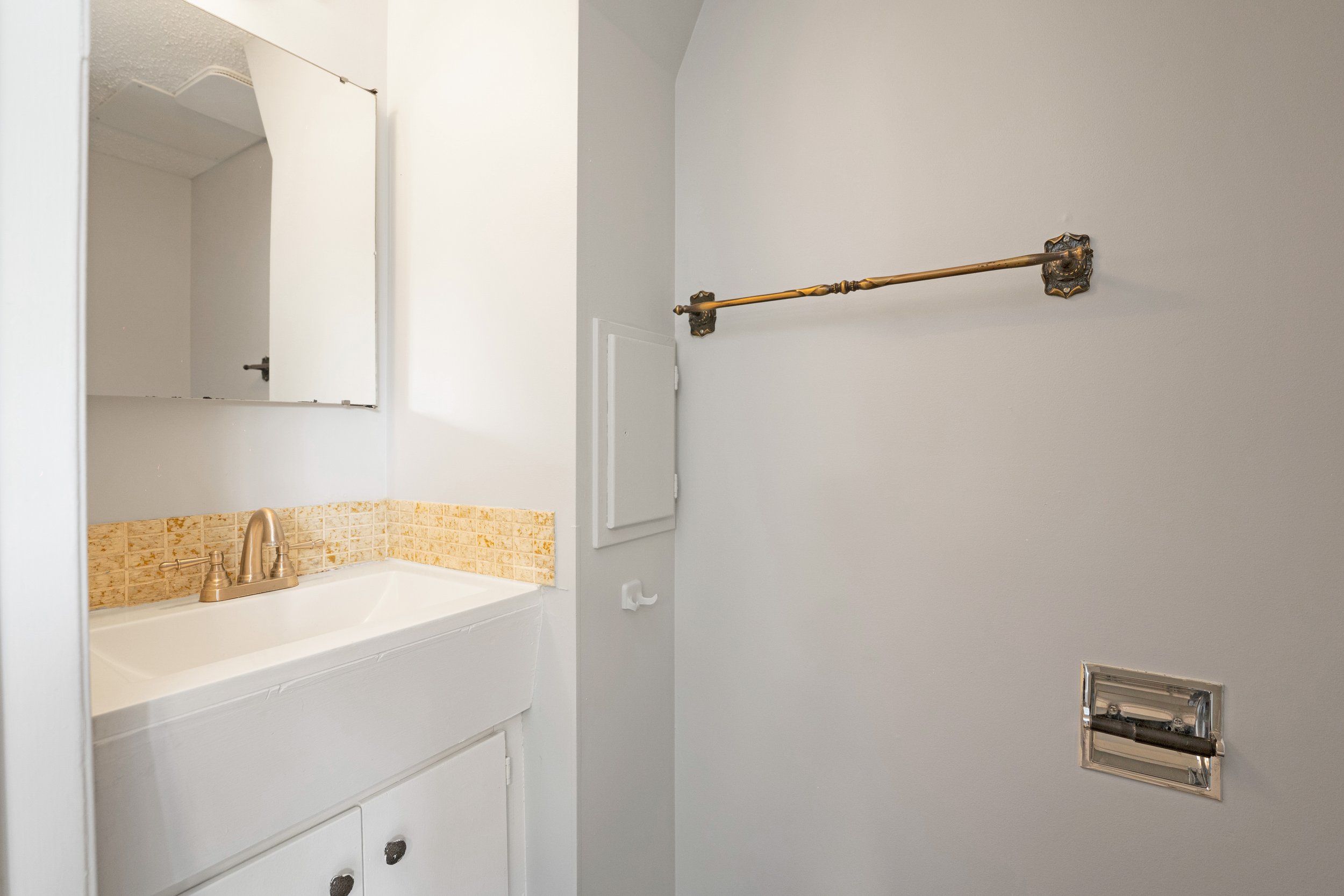 Empty bathroom or laundry room with a wall-mounted mirror, small sink with a beige countertop, a faucet, and a towel bar on the blank wall.