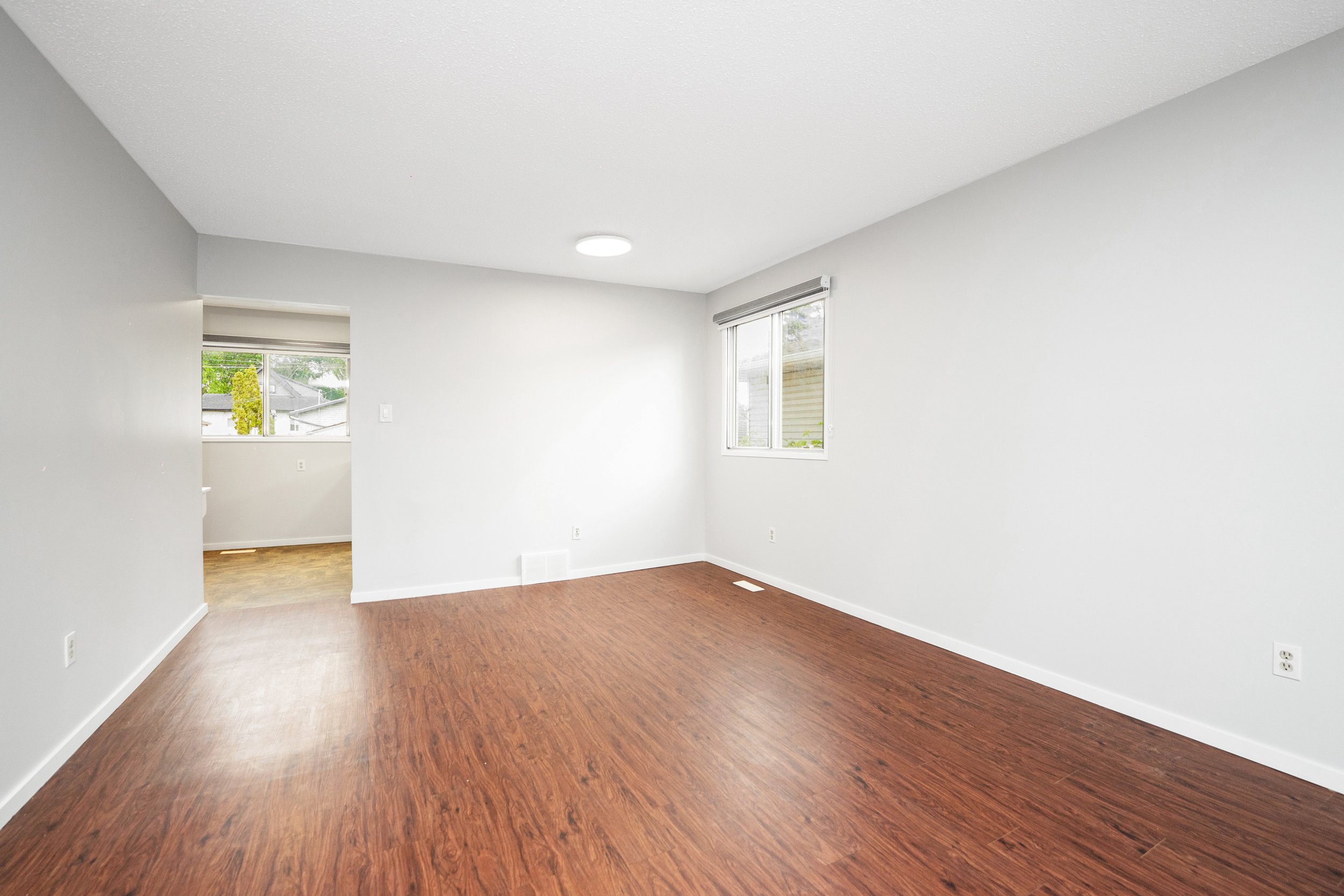 Empty room with white walls, hardwood flooring, and two windows with blinds.