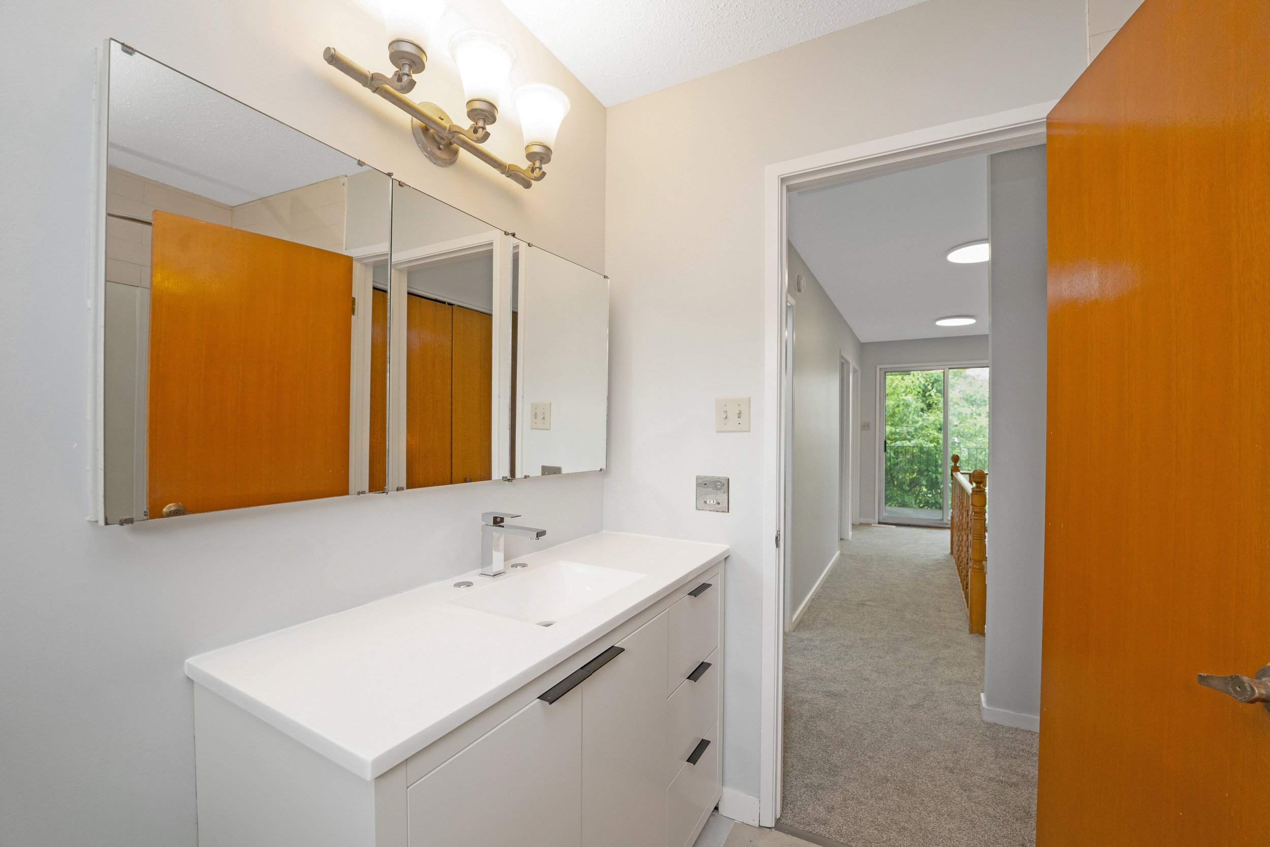 Bathroom with a large mirror, white vanity with a modern faucet, and a light fixture with four bulbs above