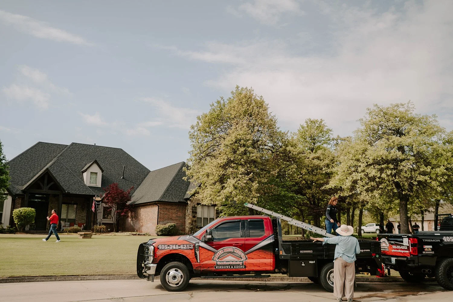 Red and black window-cleaning service truck parked outside a suburban brick home with workers and a ladder.