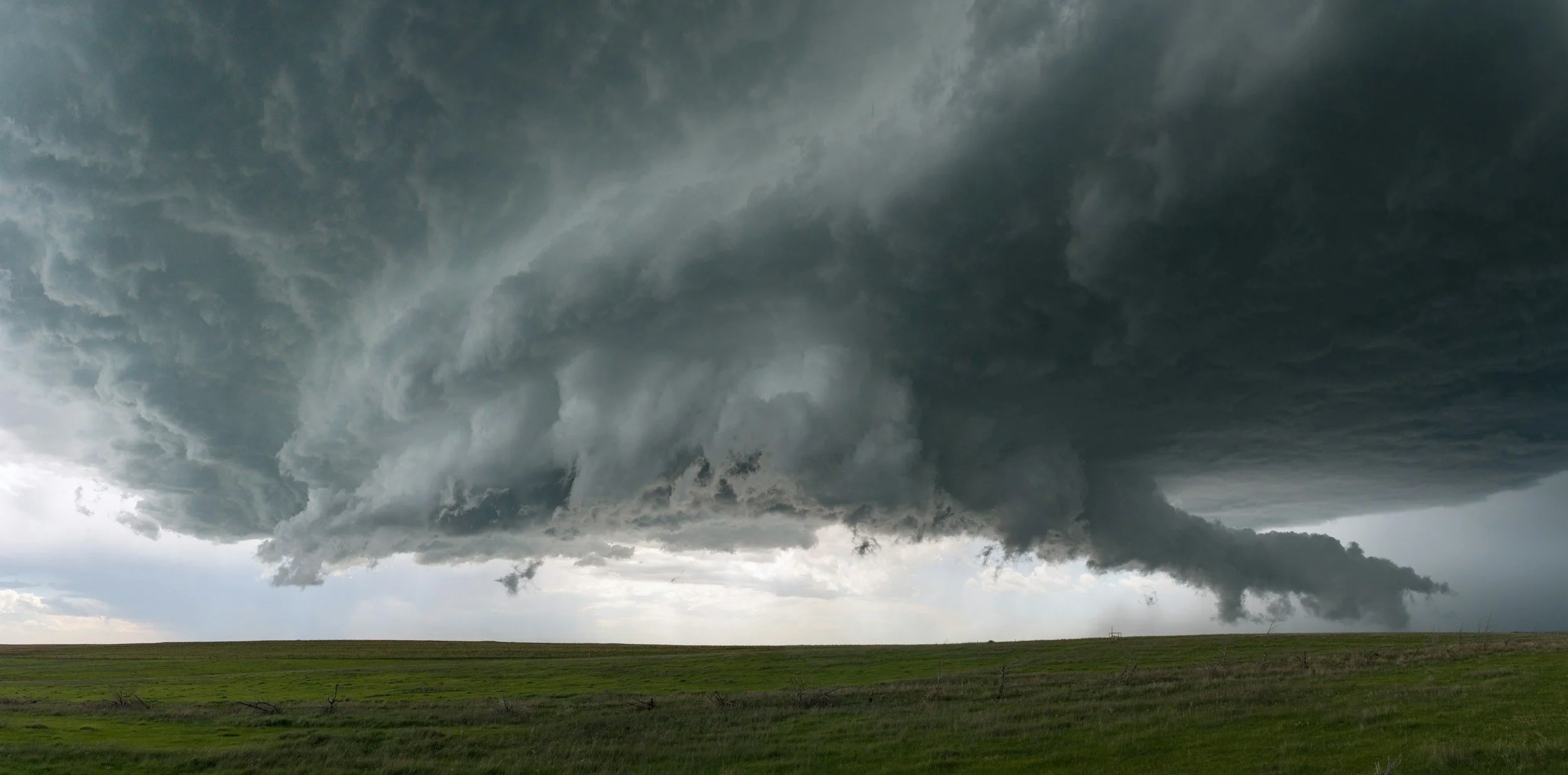 Massive dark supercell thunderstorm clouds over a flat green prairie landscape