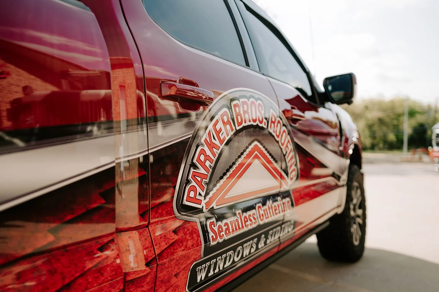 Close-up of a red Parker Bros. Windows & Siding service truck with a business logo decal