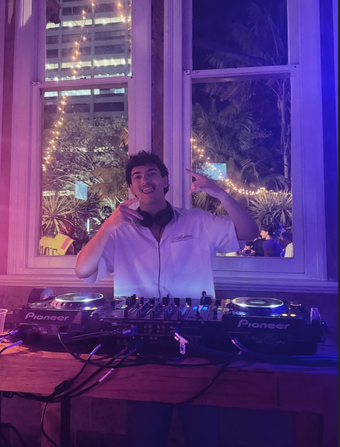 DJ performing at an evening event with warm and violet lighting.