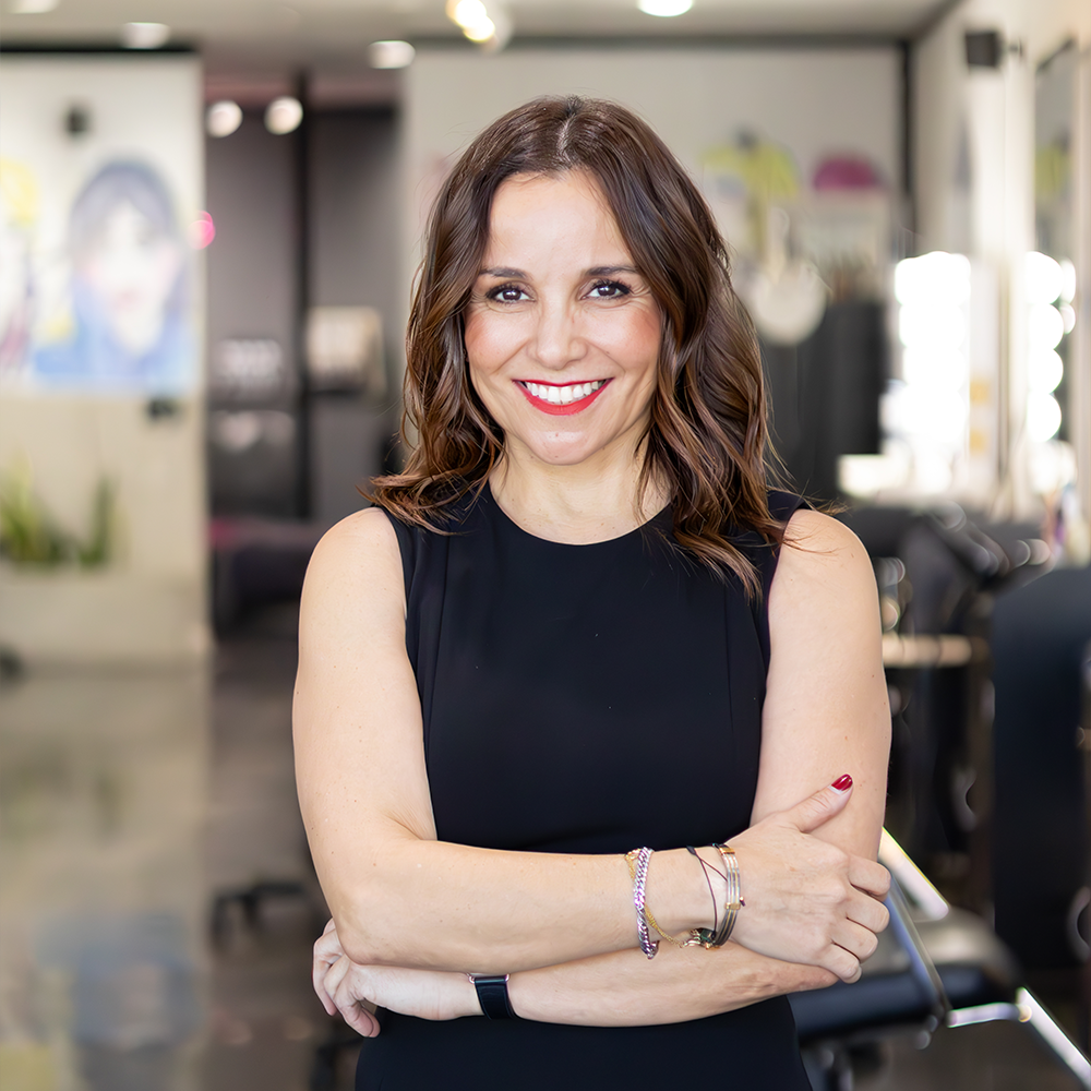 Smiling woman in a black dress standing in a modern salon.