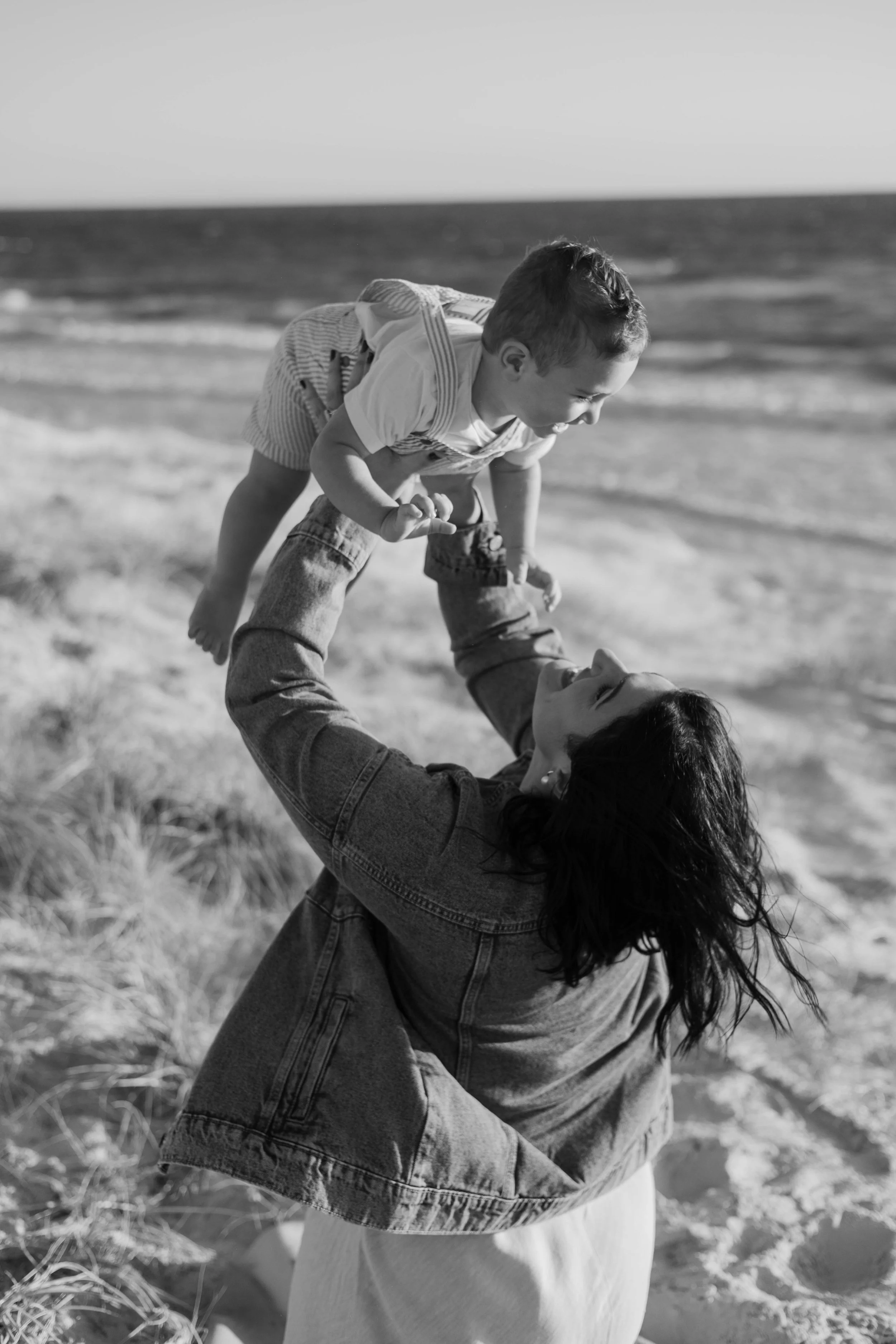 A woman playing with a young boy on the beach near the ocean in black and white.
