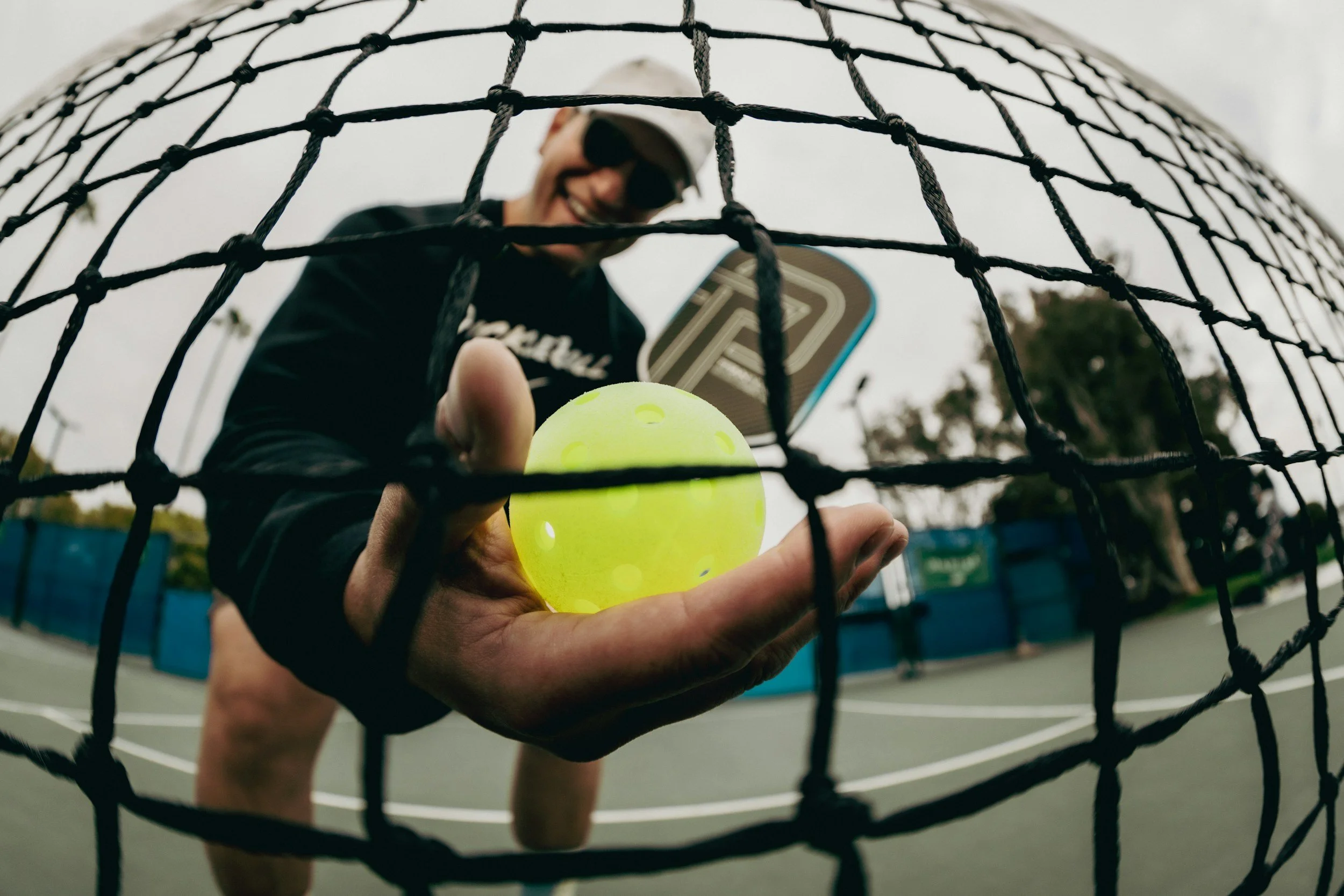 Man holding a pickleball next to a net