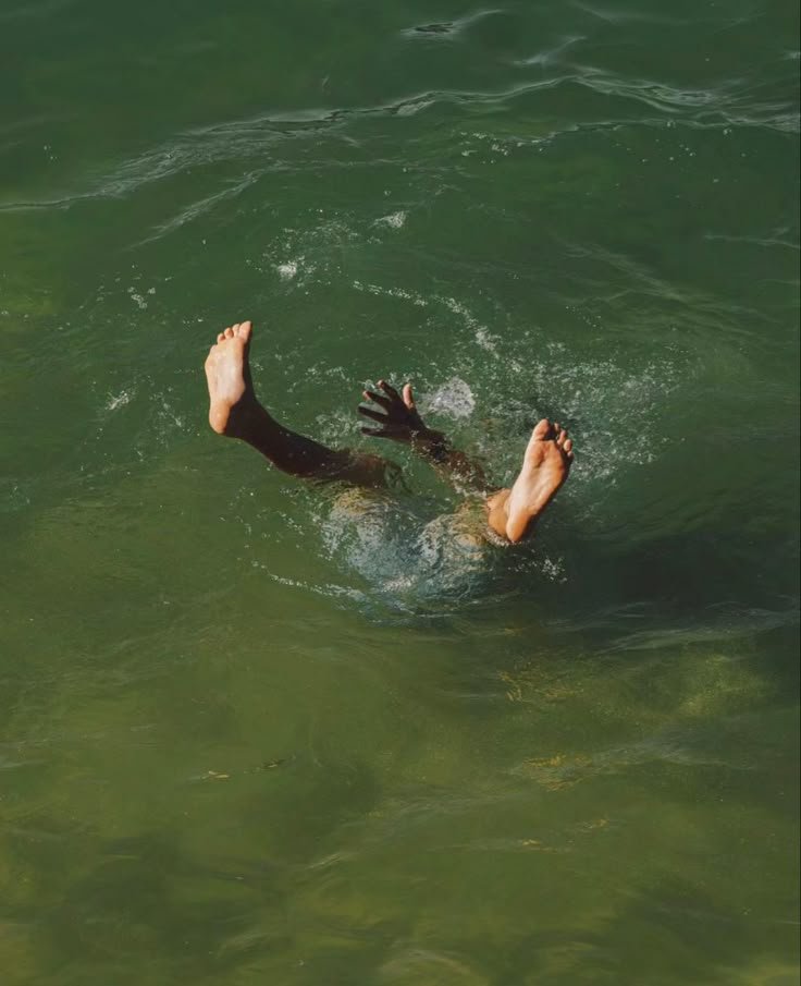 Person diving underwater in green ocean, only feet visible above surface.