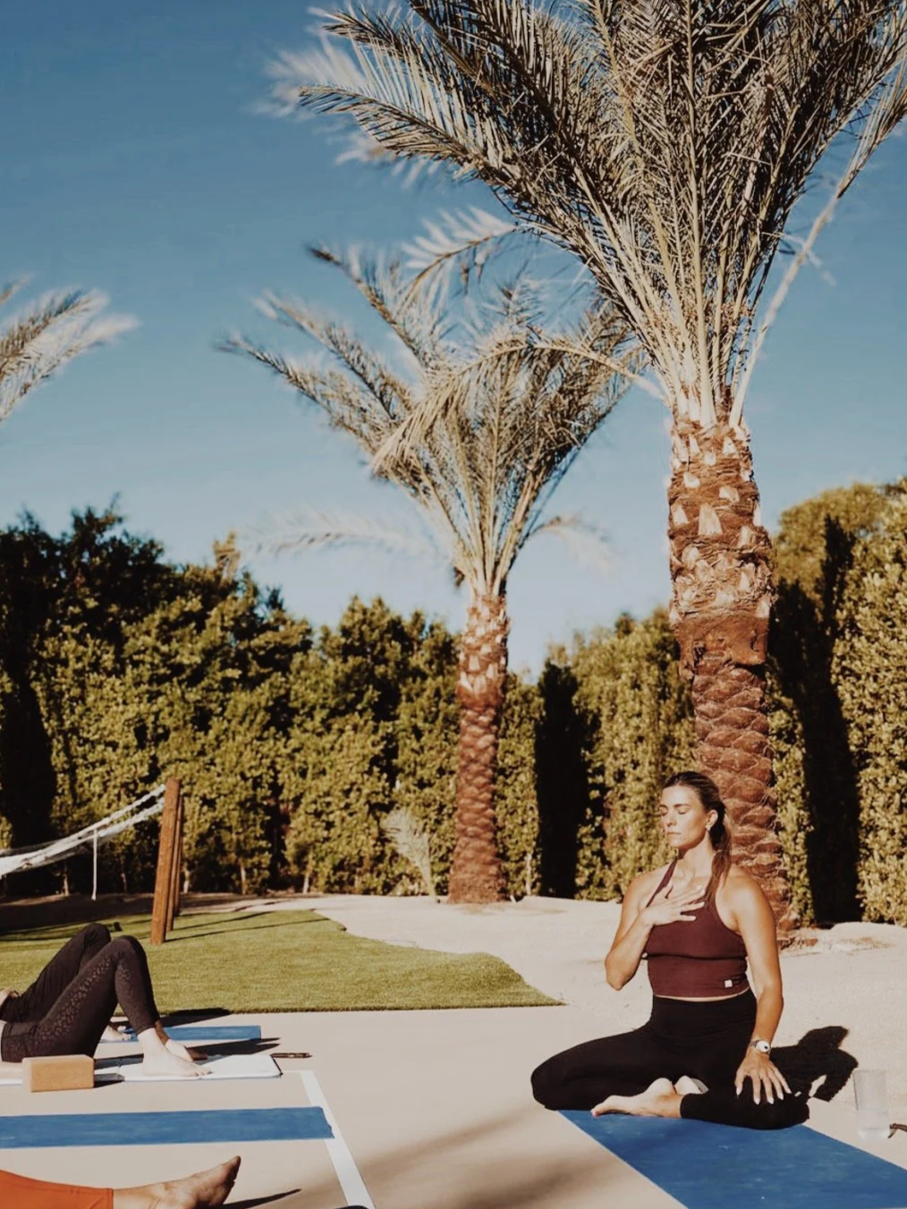 Nicole Sciacca mindful movement  day retreat outdoors on a yoga mat under tall palm trees with green foliage and a blue sky.