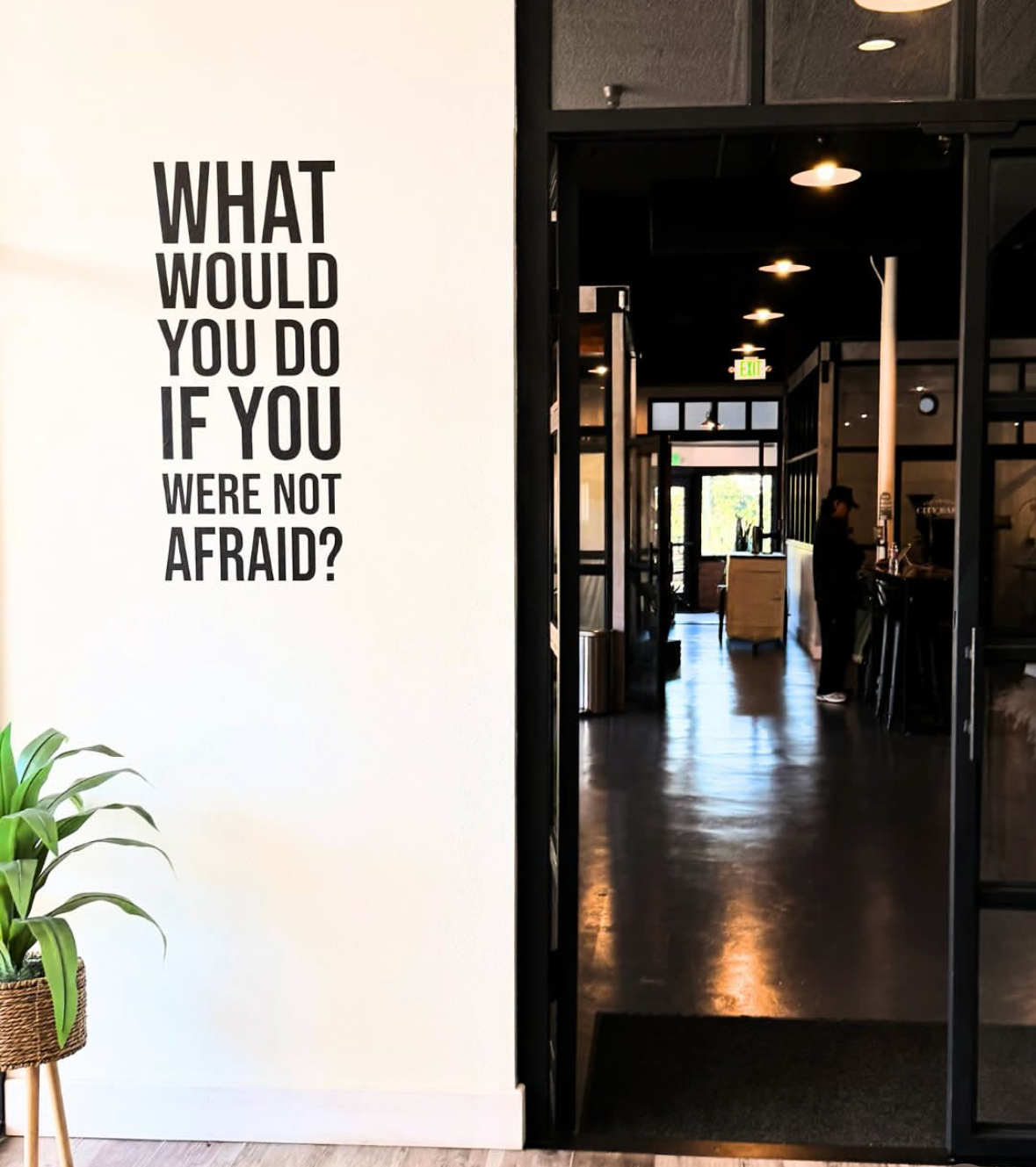 A large sign on a white wall reads, 'What would you do if you were not afraid?' in bold black letters.
