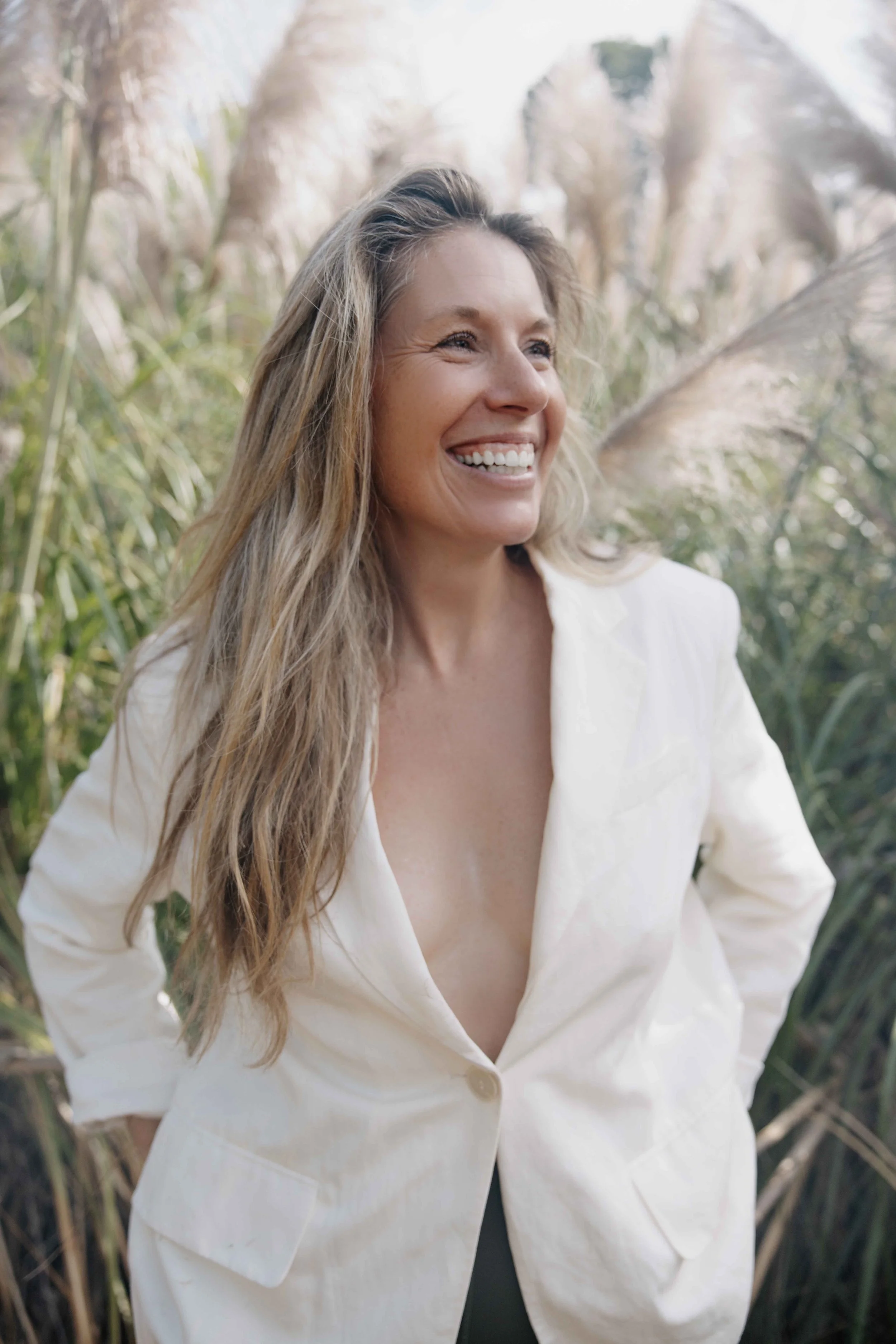 Samantha Warner Founder of The Unfiltered Life Co. wavy blonde hair, wearing a cream-colored blazer, smiling in a natural outdoor setting with tall grasses in the background.