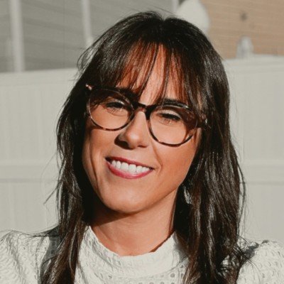 Smiling woman with dark hair, glasses, and white sweater outdoors