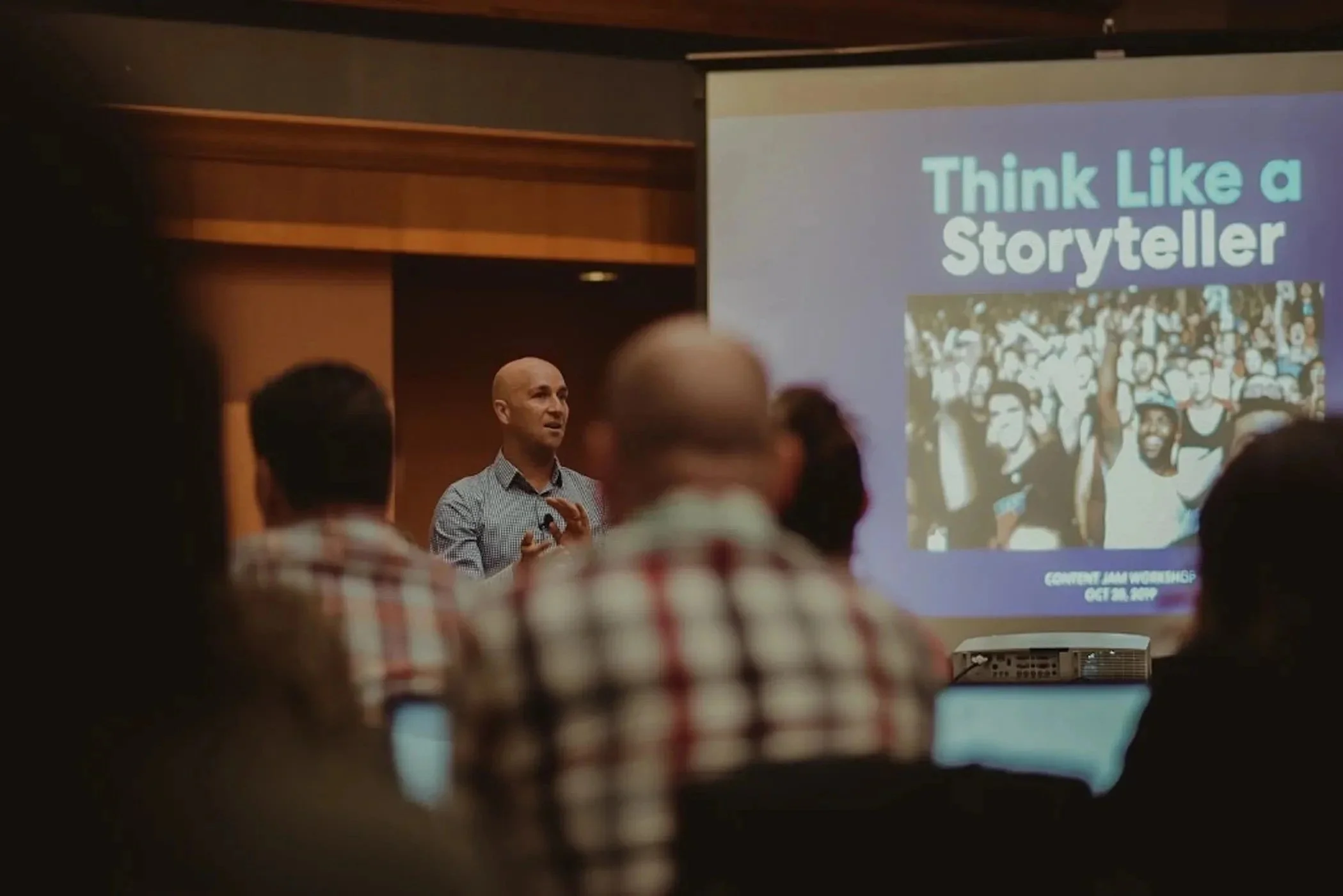 A presenter giving a talk at an event titled "Think Like a Storyteller" to an audience in a conference room.