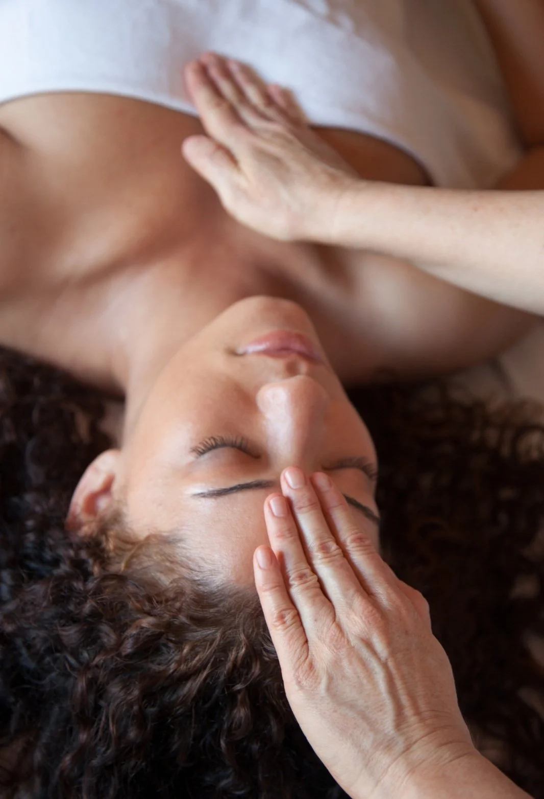 A woman with curly hair receives a forehead massage with her eyes closed.