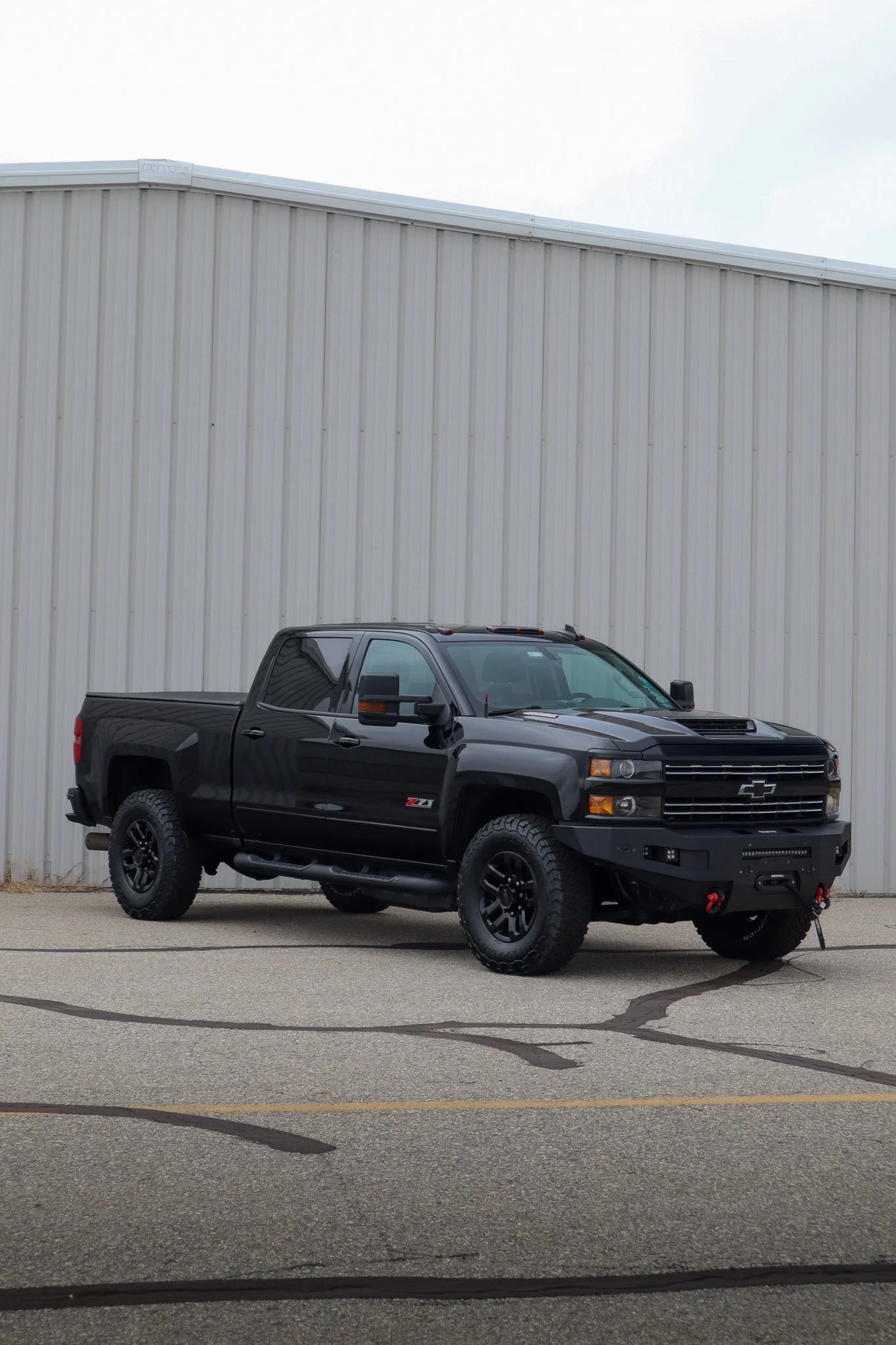 A black Chevrolet Silverado pickup truck parked on a paved lot in front of a large beige metal building.