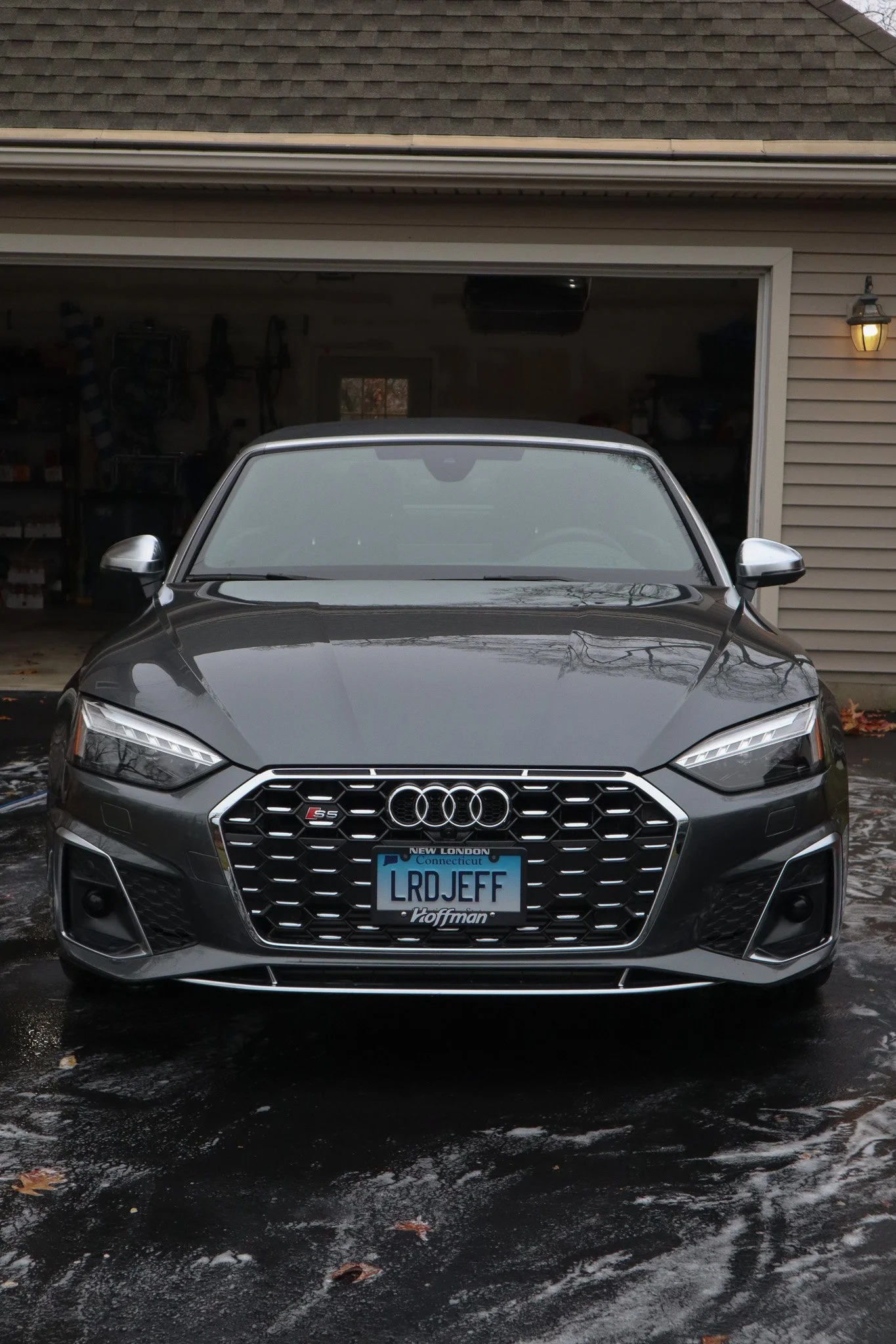 Front view of a metallic gray Audi car parked in front of a garage with the license plate reading 'LRD JEFF'.