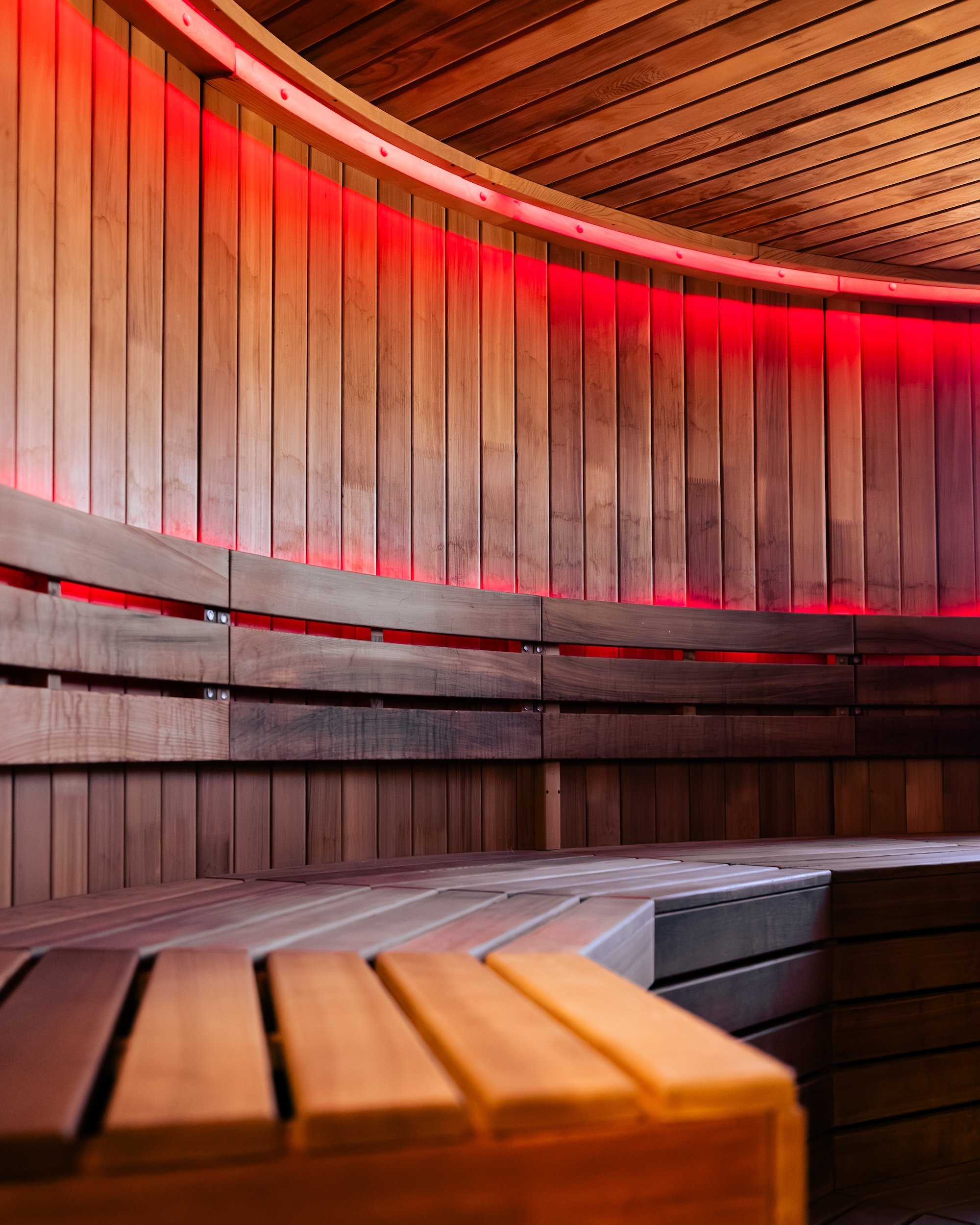 Interior of a wooden sauna with curved benches and red lighting along the walls.