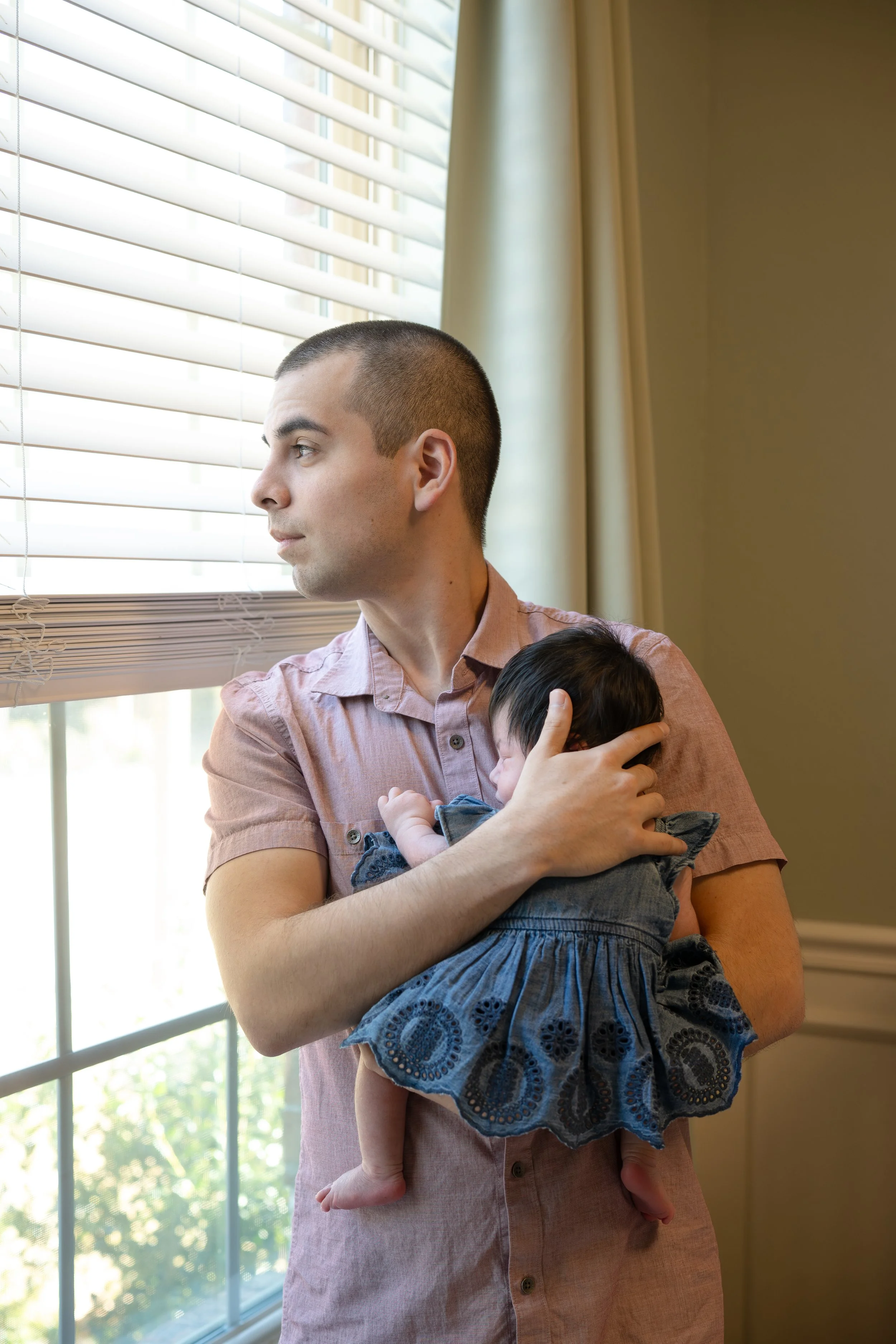 houston dad holding newborn daughter baby at home and looking out of the window