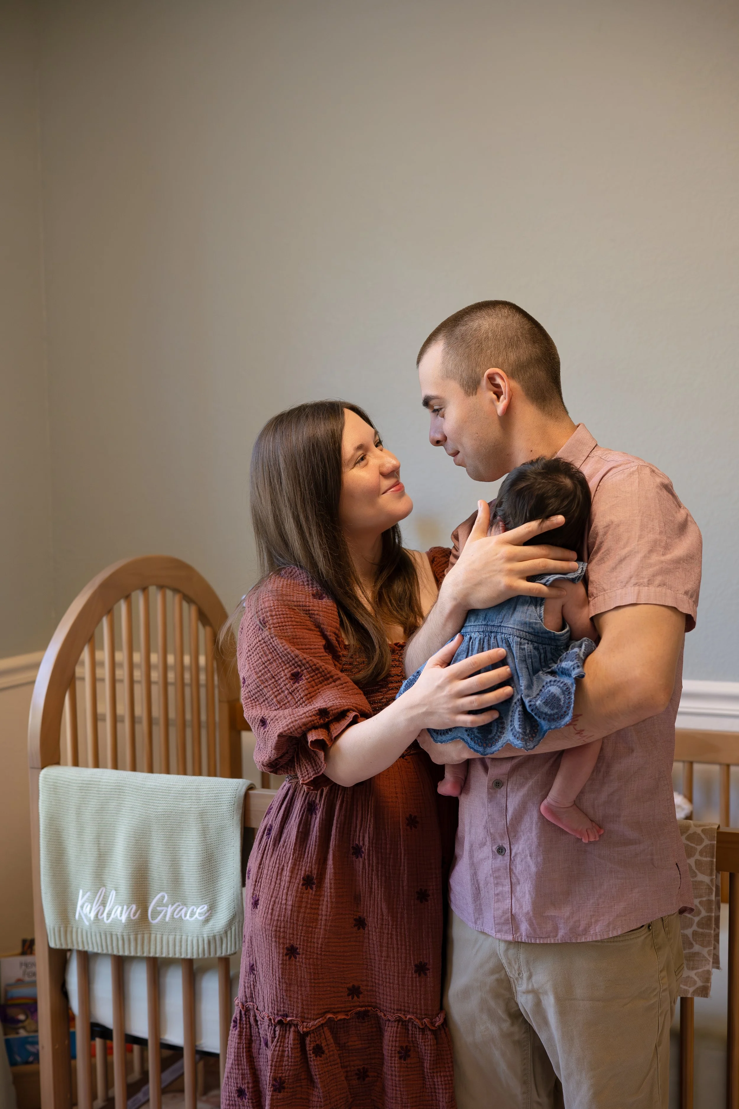houston mom & dad holding baby next to crib at home smiling together