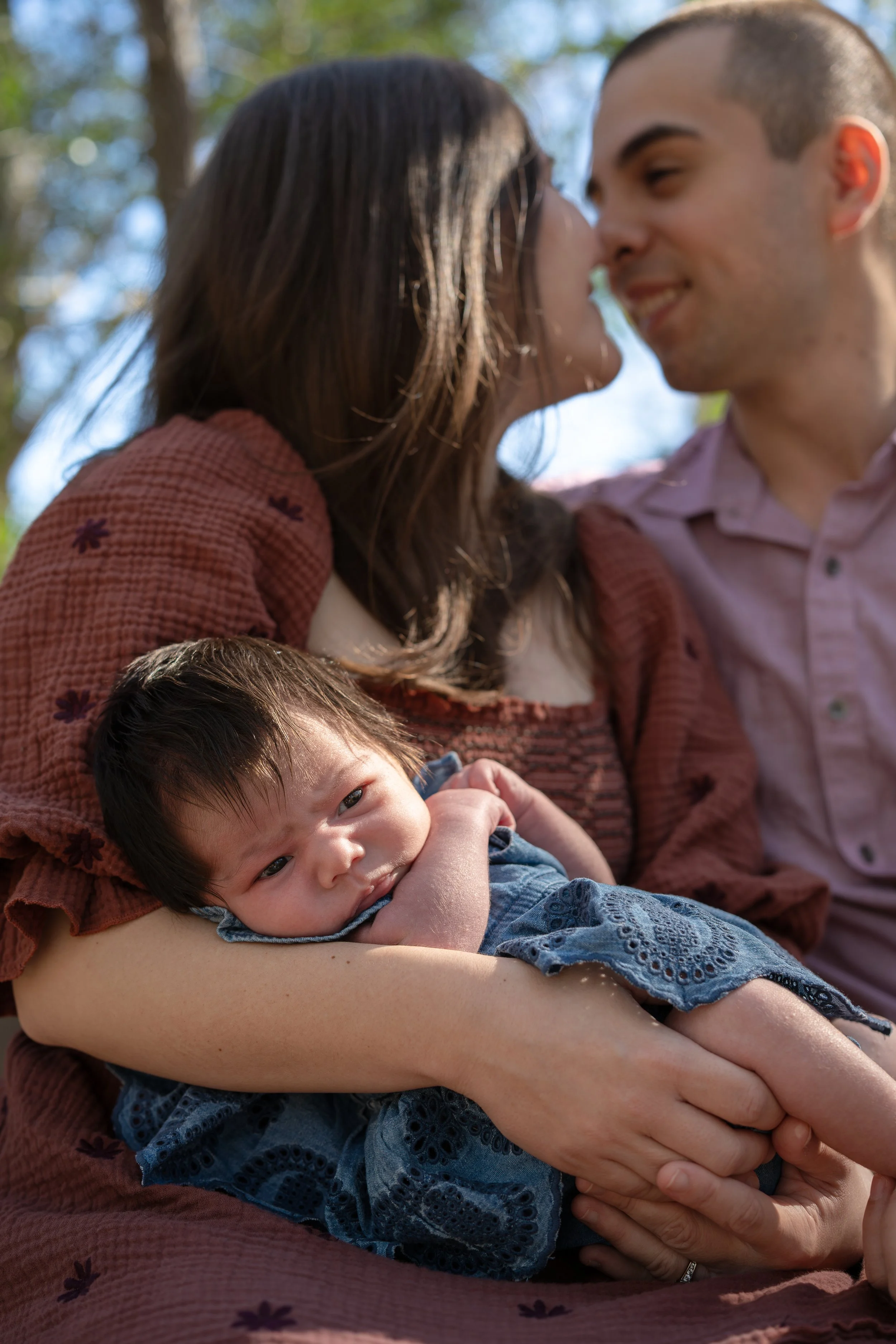 houston mom & dad smiling at each other while mom is holding newborn baby at home outside