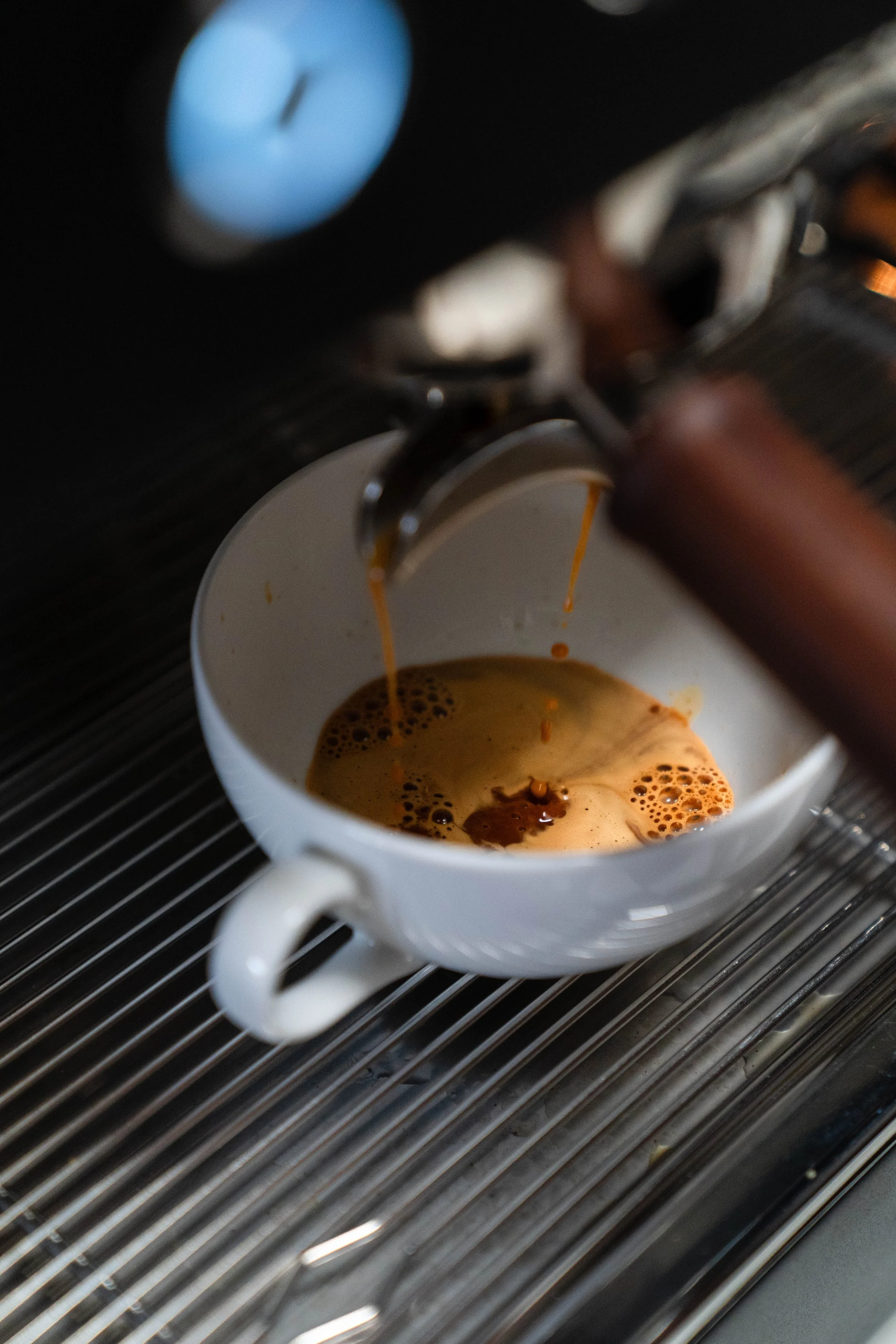 A white ceramic coffee mug under a coffee machine spout, with espresso brewing into the mug. The mug is on a metal drip tray.
