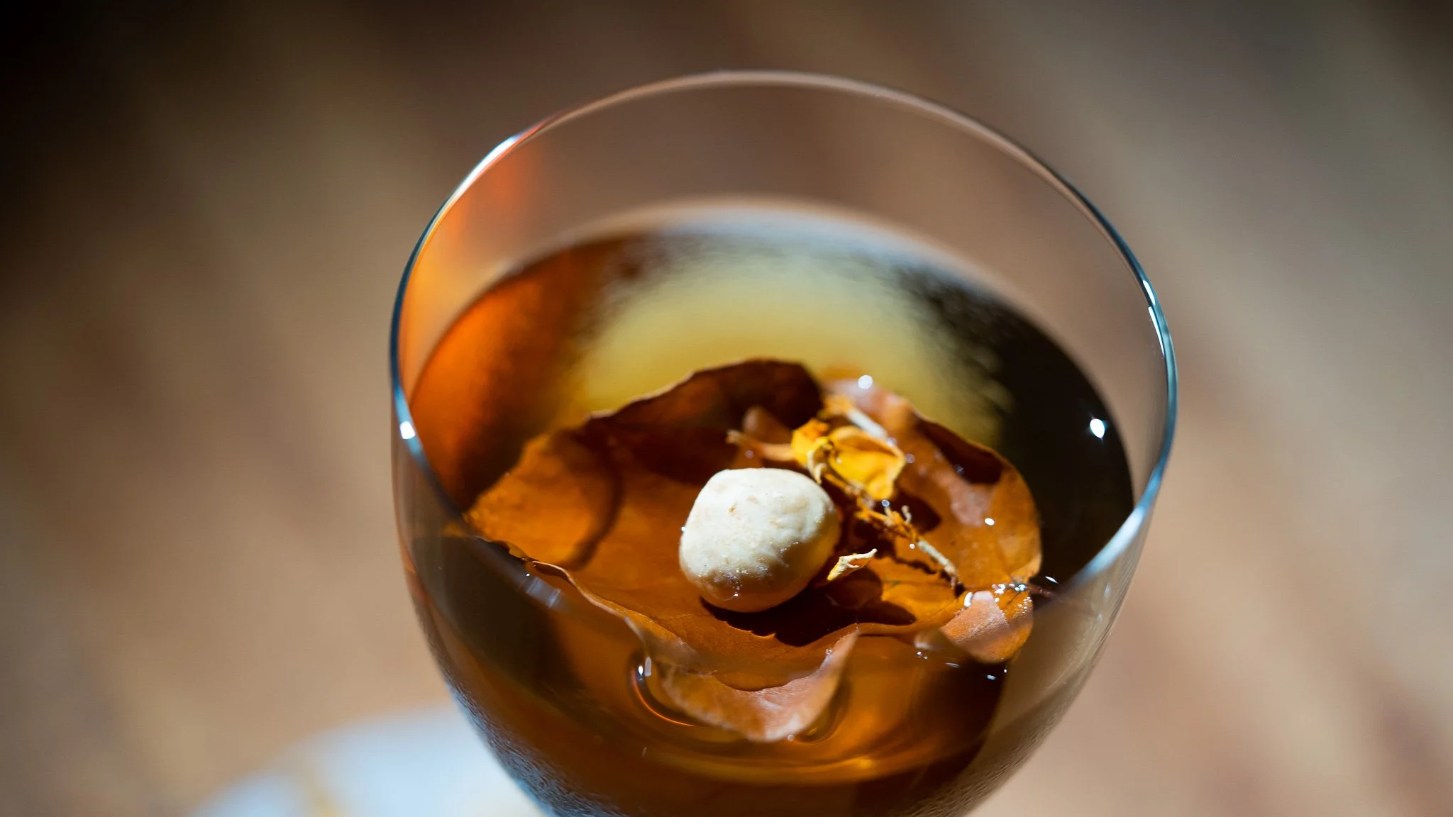 A glass of dark liquid, likely ice tea or soda, with floating ice and a large dried leaf as garnish.