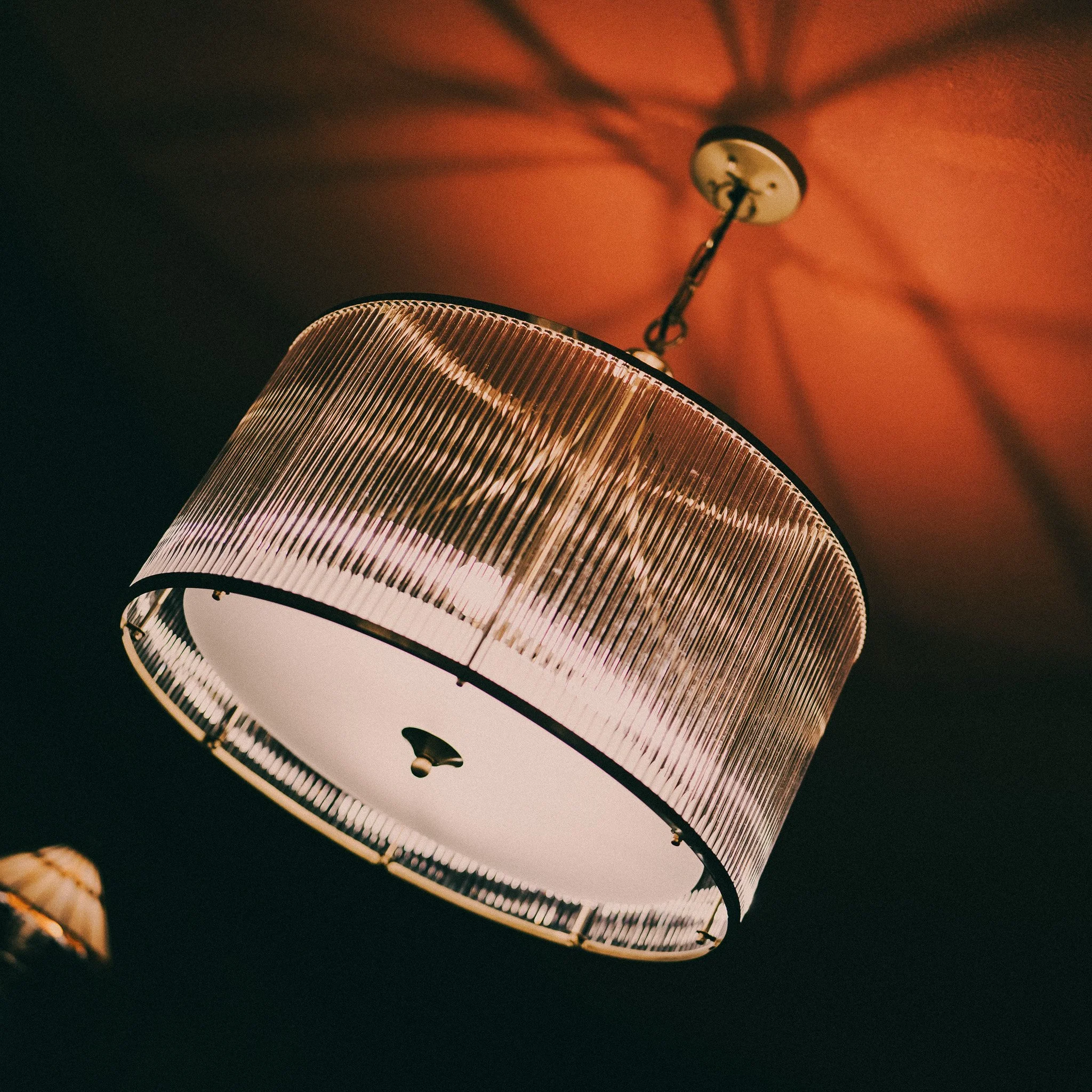 A modern pendant ceiling light with a ribbed glass shade, mounted on a ceiling with a warm orange glow.