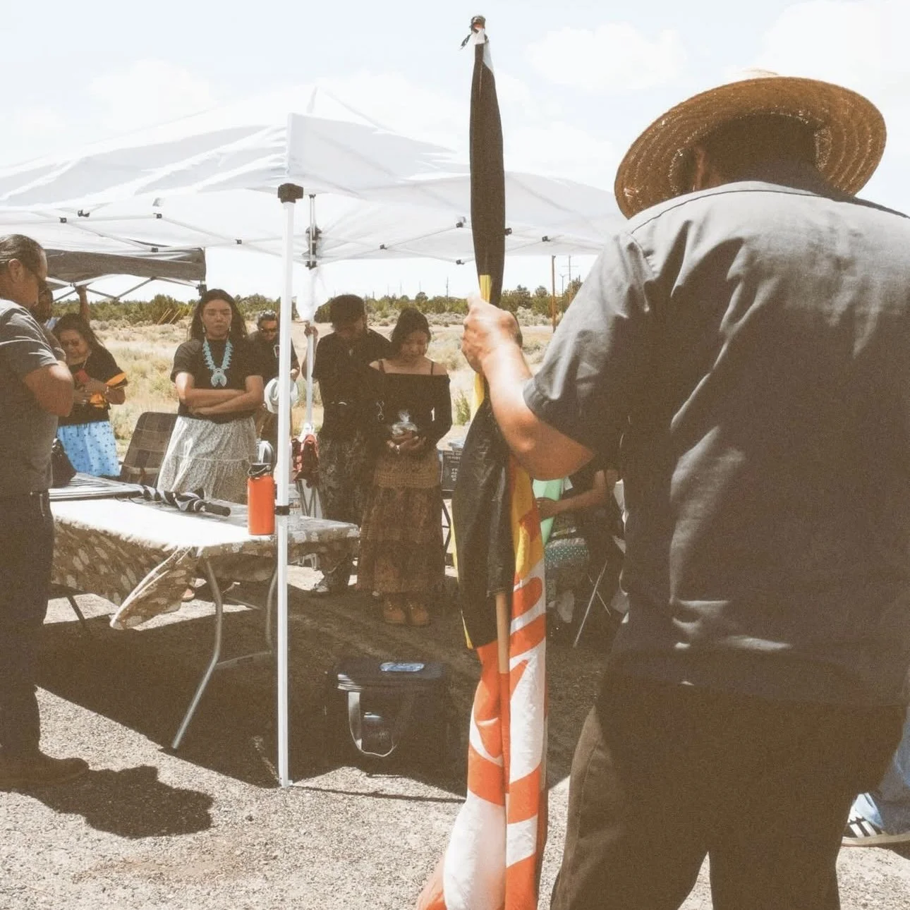 Group of people gathered outdoors under tents, with Activist, Louvannina Tsosie. 