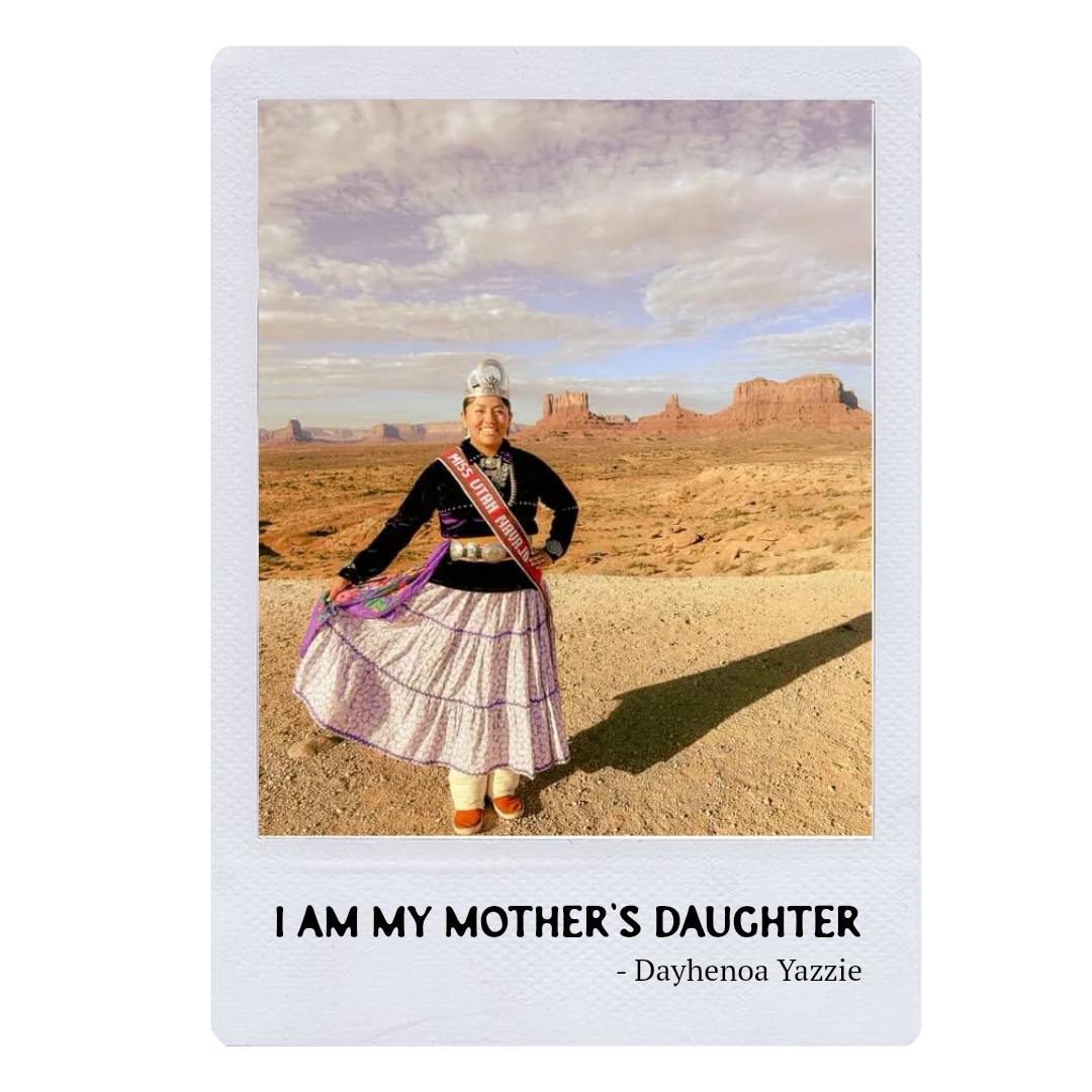 A woman in traditional Native American attire standing in a desert landscape with rock formations and cloudy sky in the background.