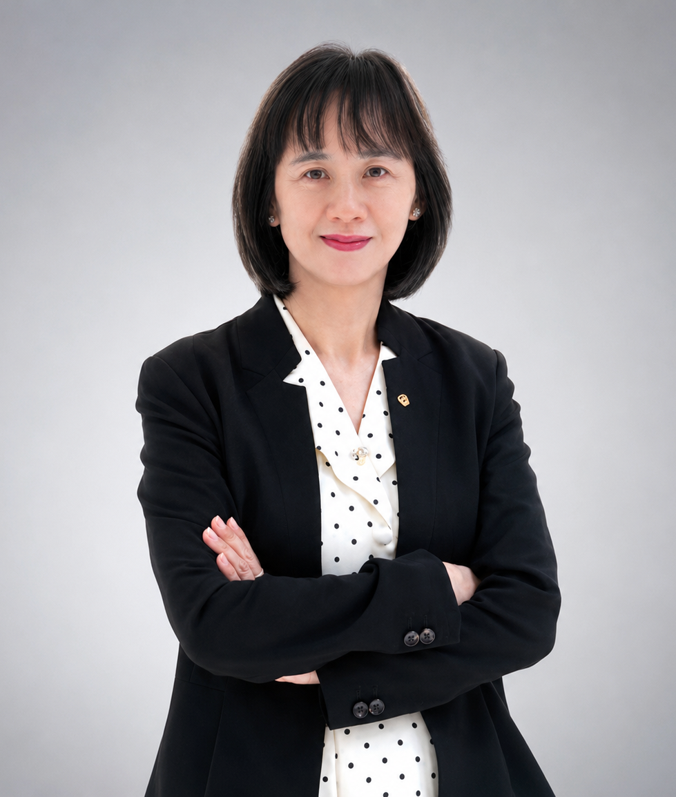 Professional woman standing with arms crossed, wearing a black blazer and a white blouse with black polka dots, against a gray background.