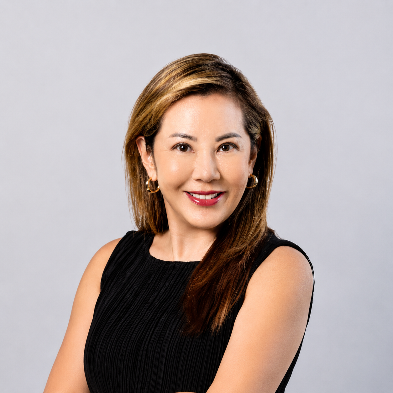 A woman with shoulder-length brown hair wearing a sleeveless black top, smiling, against a plain light gray background.