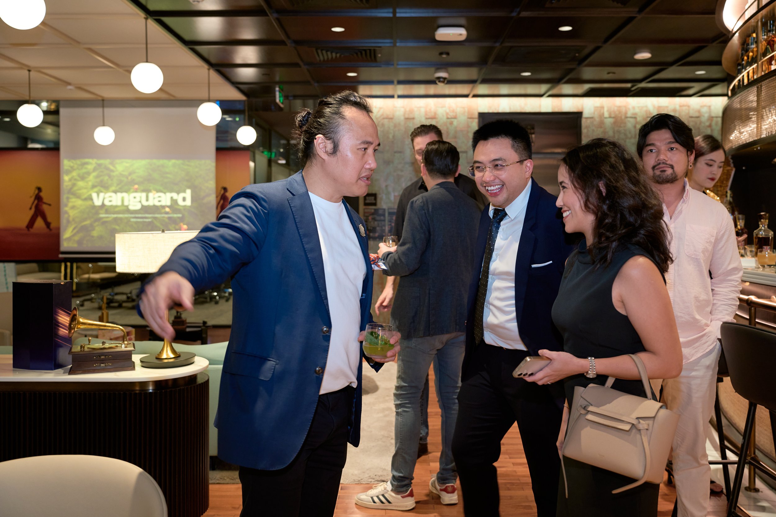 People socializing at a networking event with a 'vanguard' presentation screen in the background.