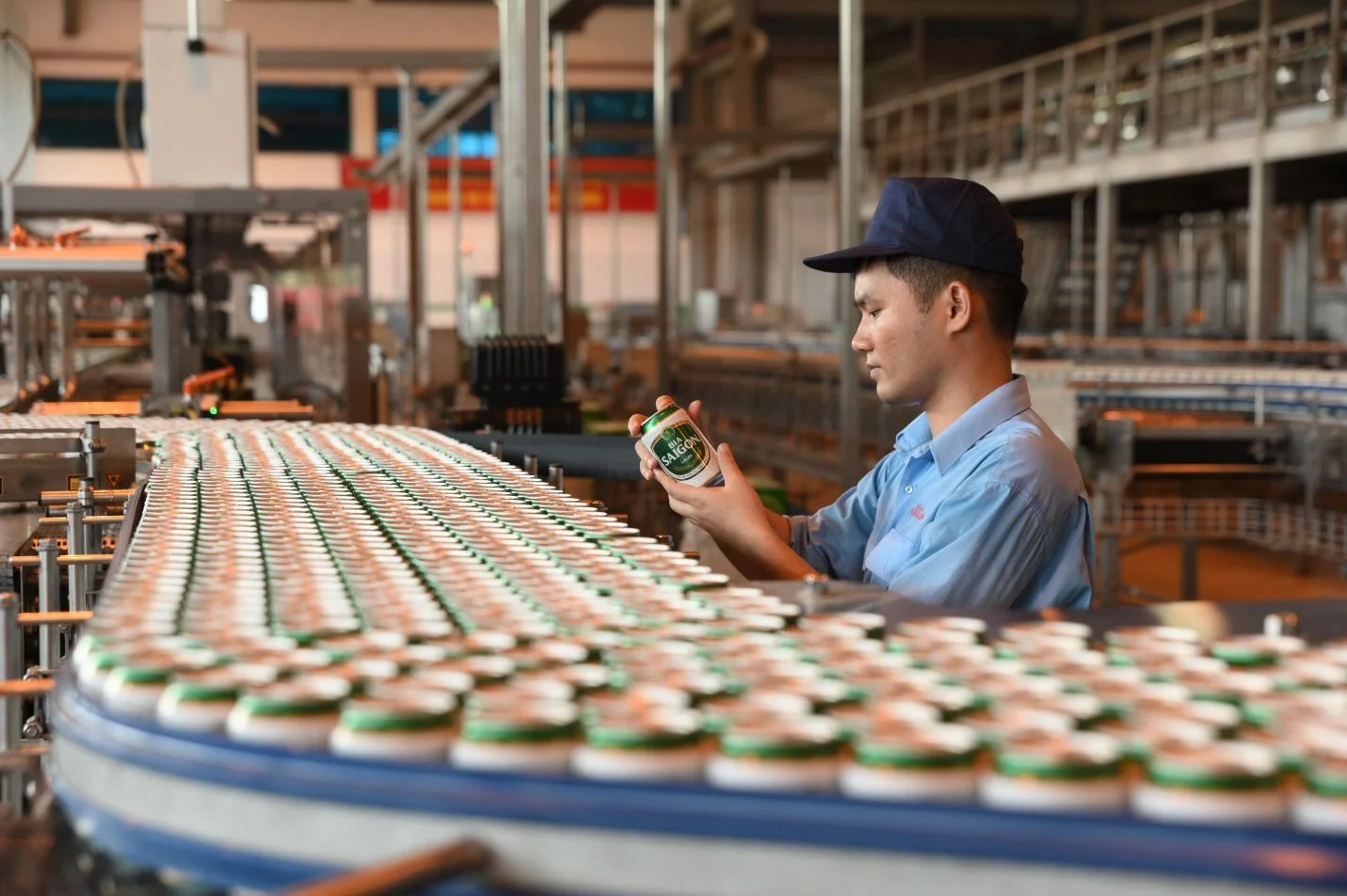 A worker in a factory examining a jar of salsa near a conveyor belt filled with jars of salsa in an industrial setting.