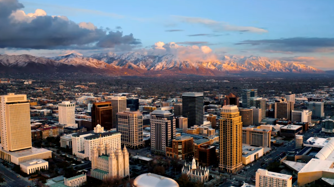 A panoramic view of a city skyline with tall buildings and mountains in the background during sunset.