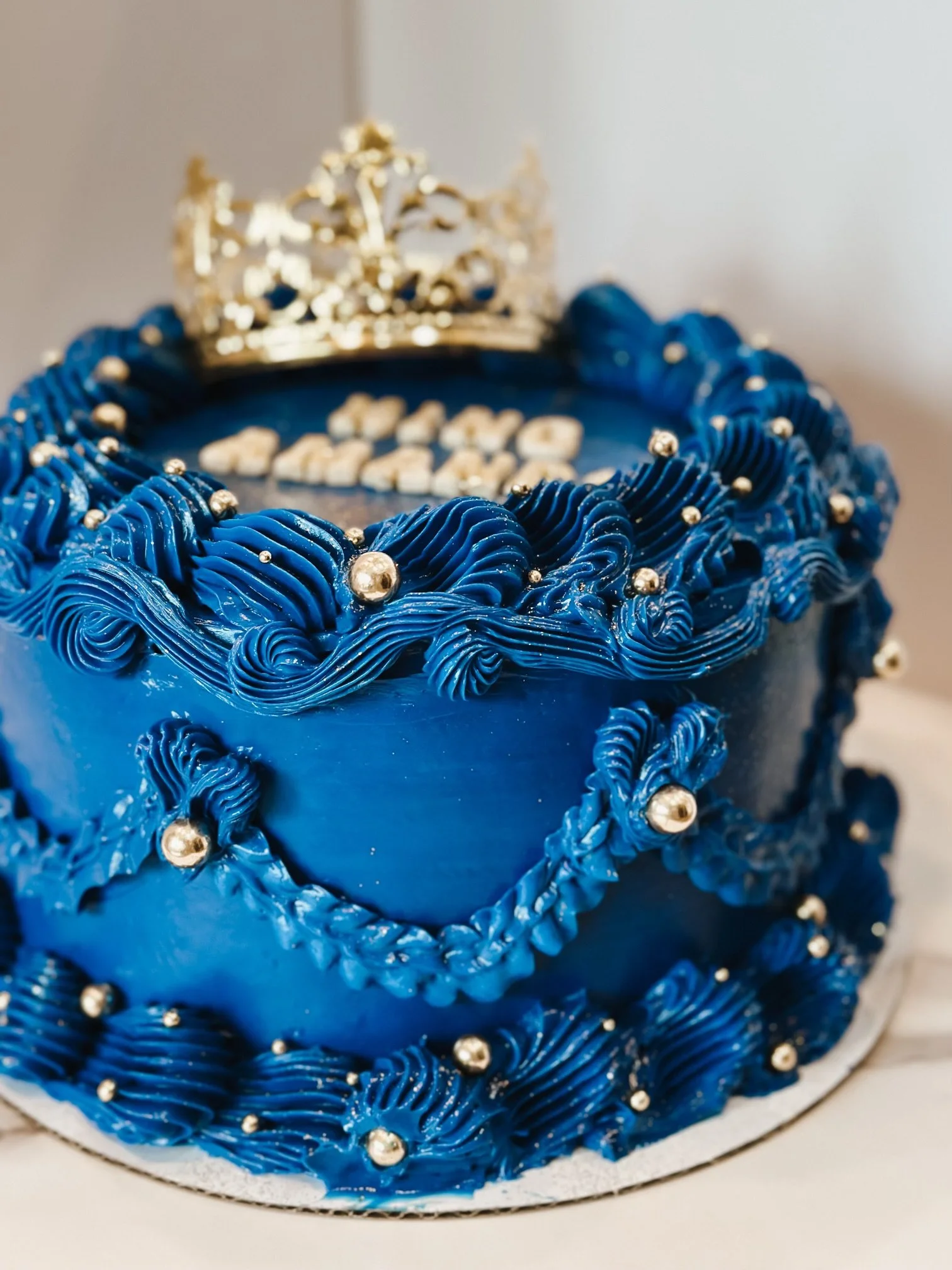 Vintage-style royal blue buttercream cake with ornate piping, edible silver pearls, and a gold tiara topper, handcrafted by Twice As Sweet OC in Huntington Beach, California.