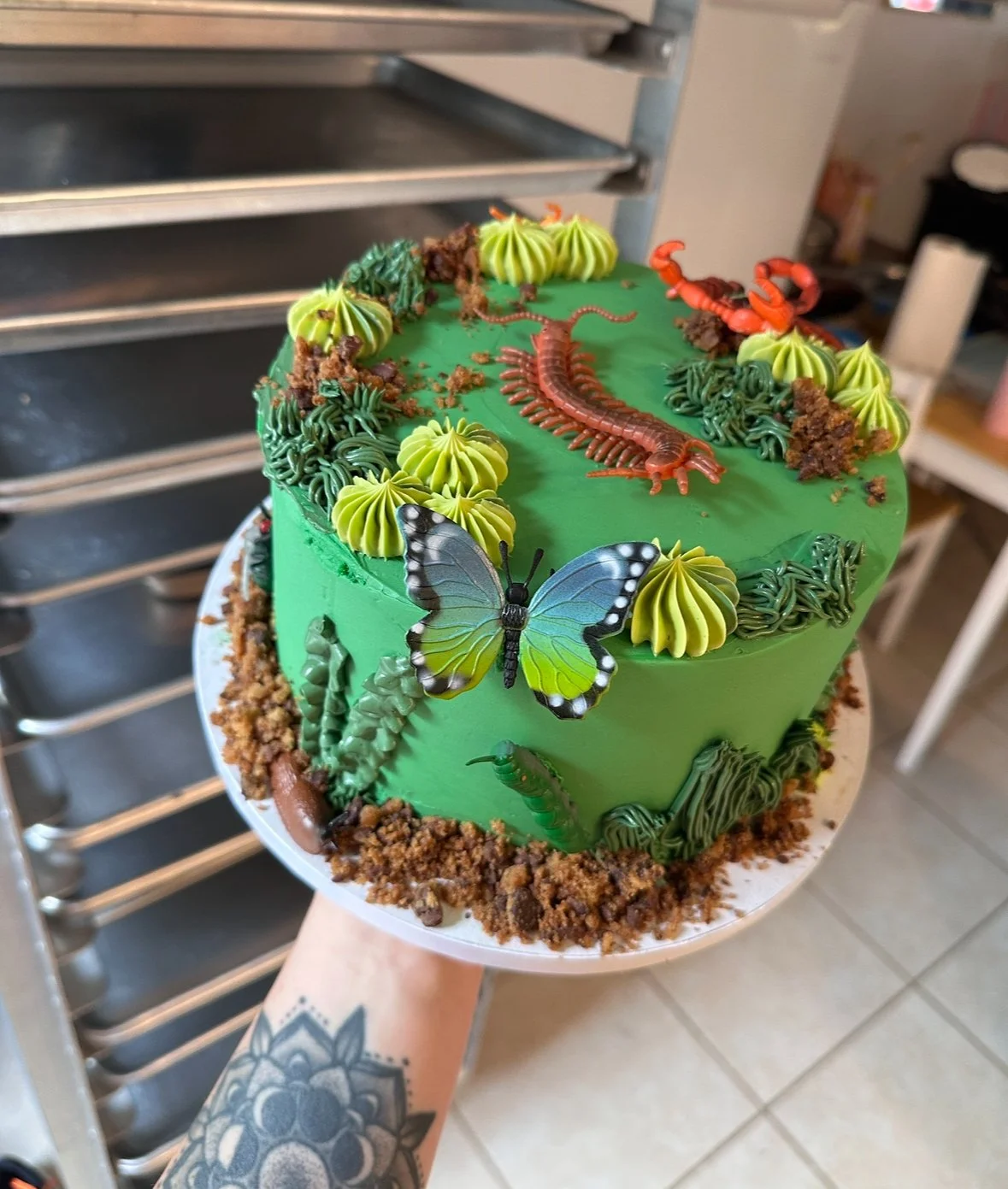 Custom bug-themed birthday cake by Twice As Sweet OC, featuring hand-piped green buttercream, edible dirt crumble, and playful details like butterflies, centipedes, and scorpions — designed for a nature-loving celebration in Huntington Beach Twice As