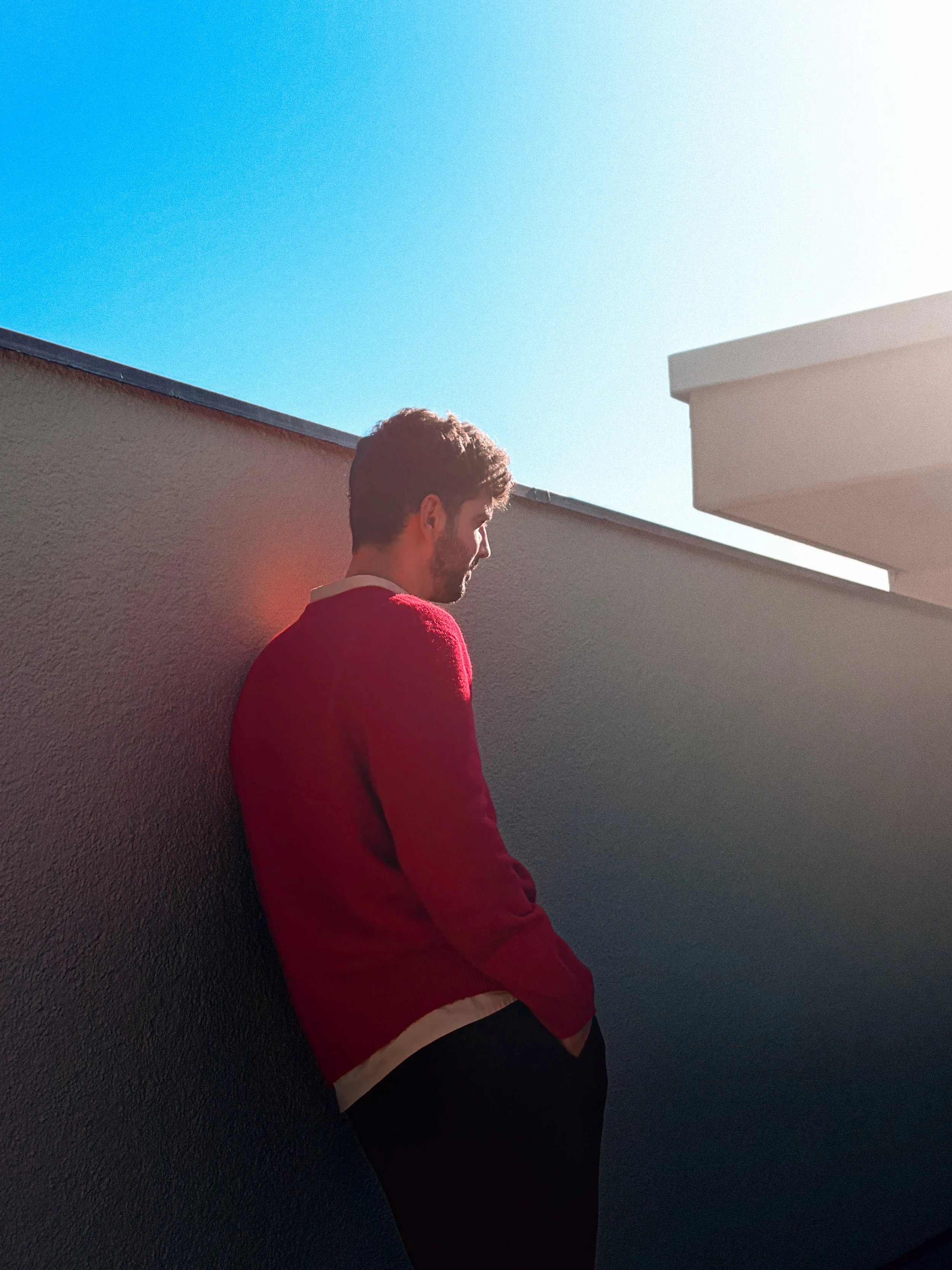 Porträt eines Mannes im roten Pullover an einer weissen Wand unter blauem Himmel